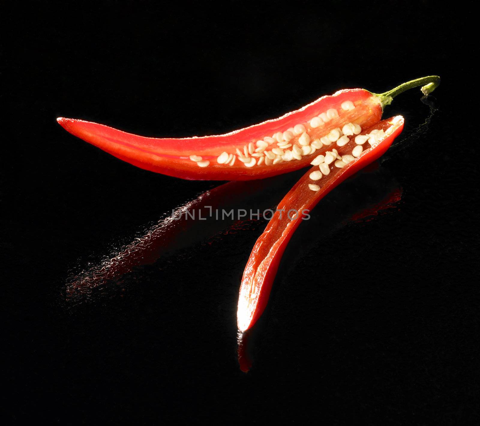 studio shot of a red sliced chili in black reflective back