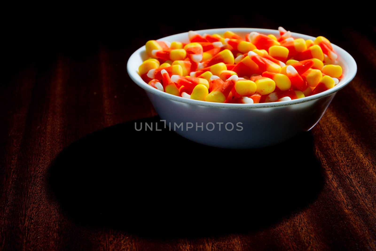 Candy corn in a bowl on a table that is lightly lit.