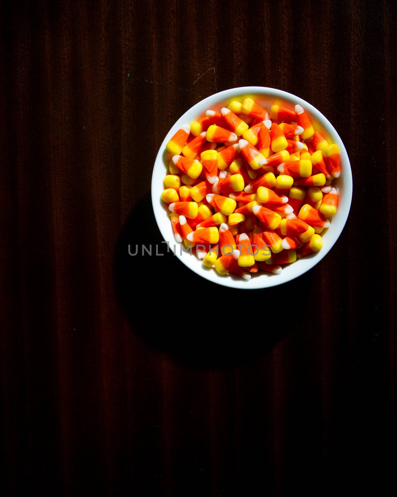 Top down view of candy corn on a dim lit wood table giving a creepy scary vibe