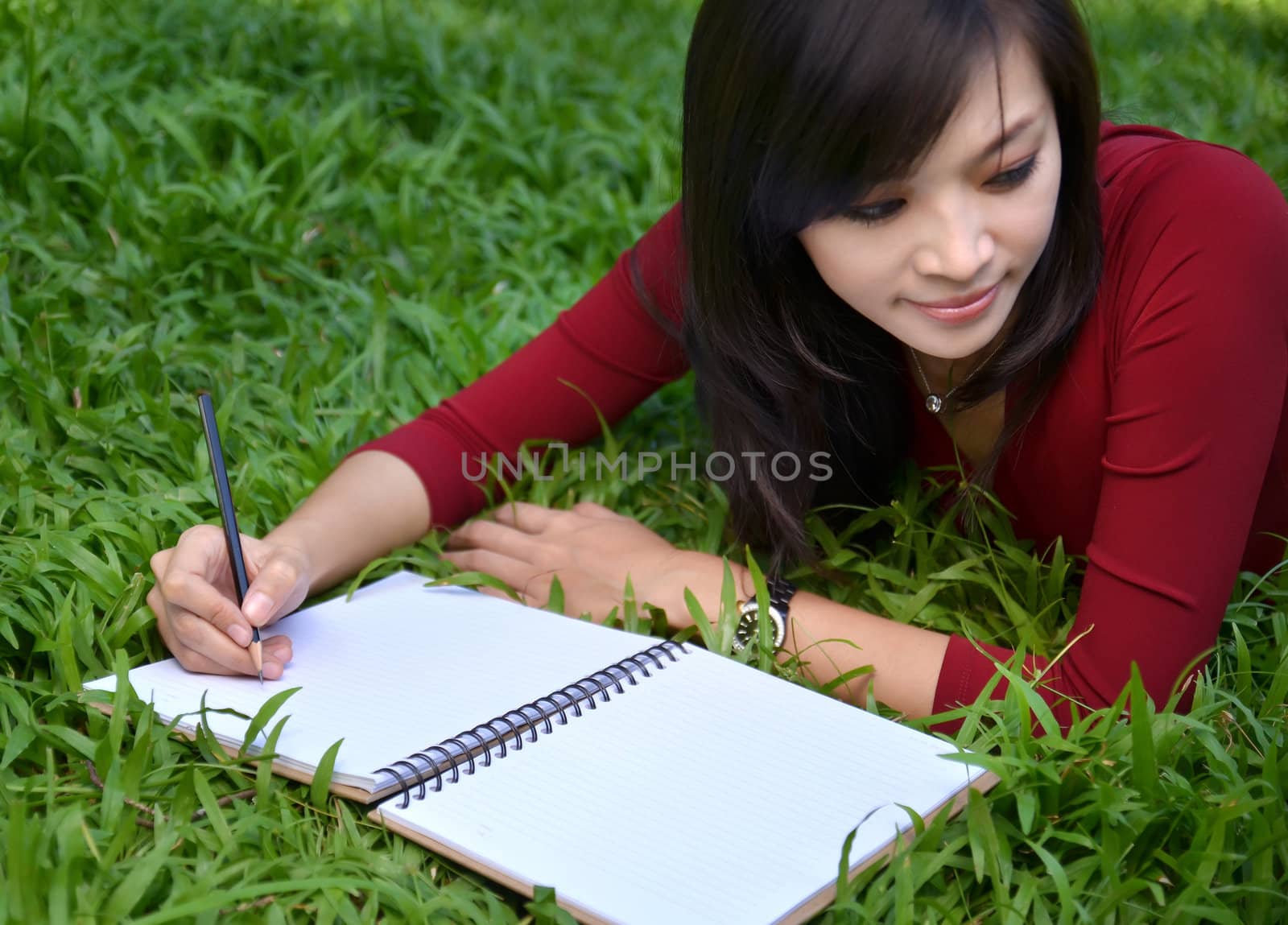 pretty women lying on green grass and writing book