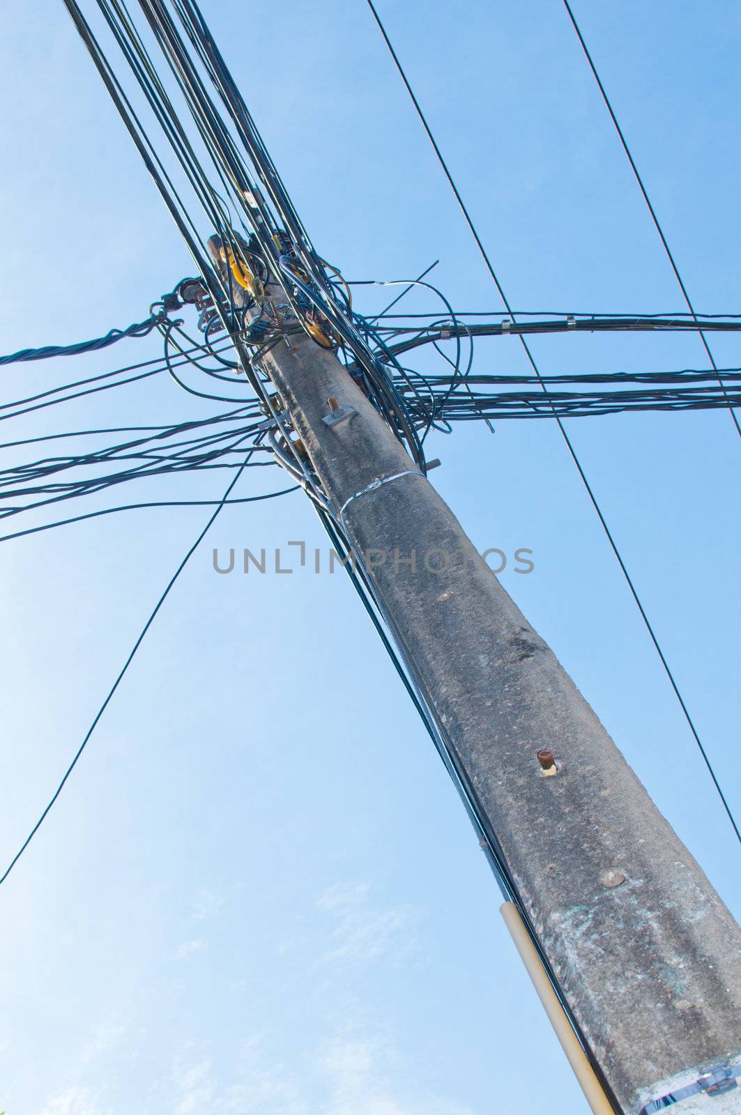 Energy and technology: electrical post by the road with power line cables, transformers and phone lines against bright blue sky providing copy space.