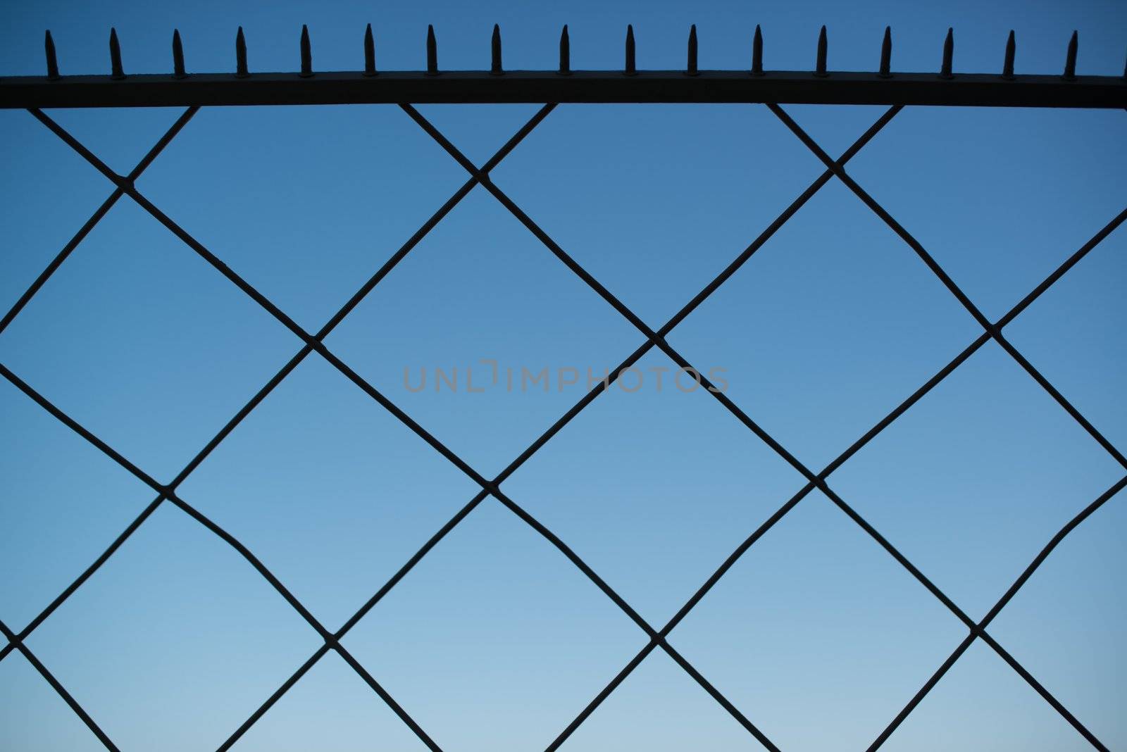Metal fence with sharp spikes at the top against great blue sky