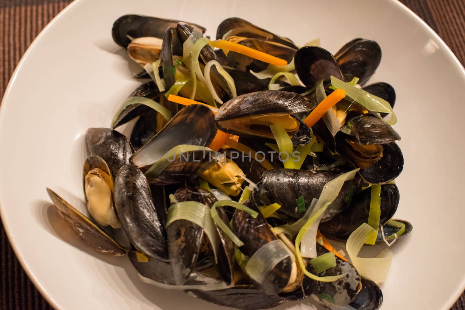Cooked mussels with white wine sauce and vegetables on a plate.