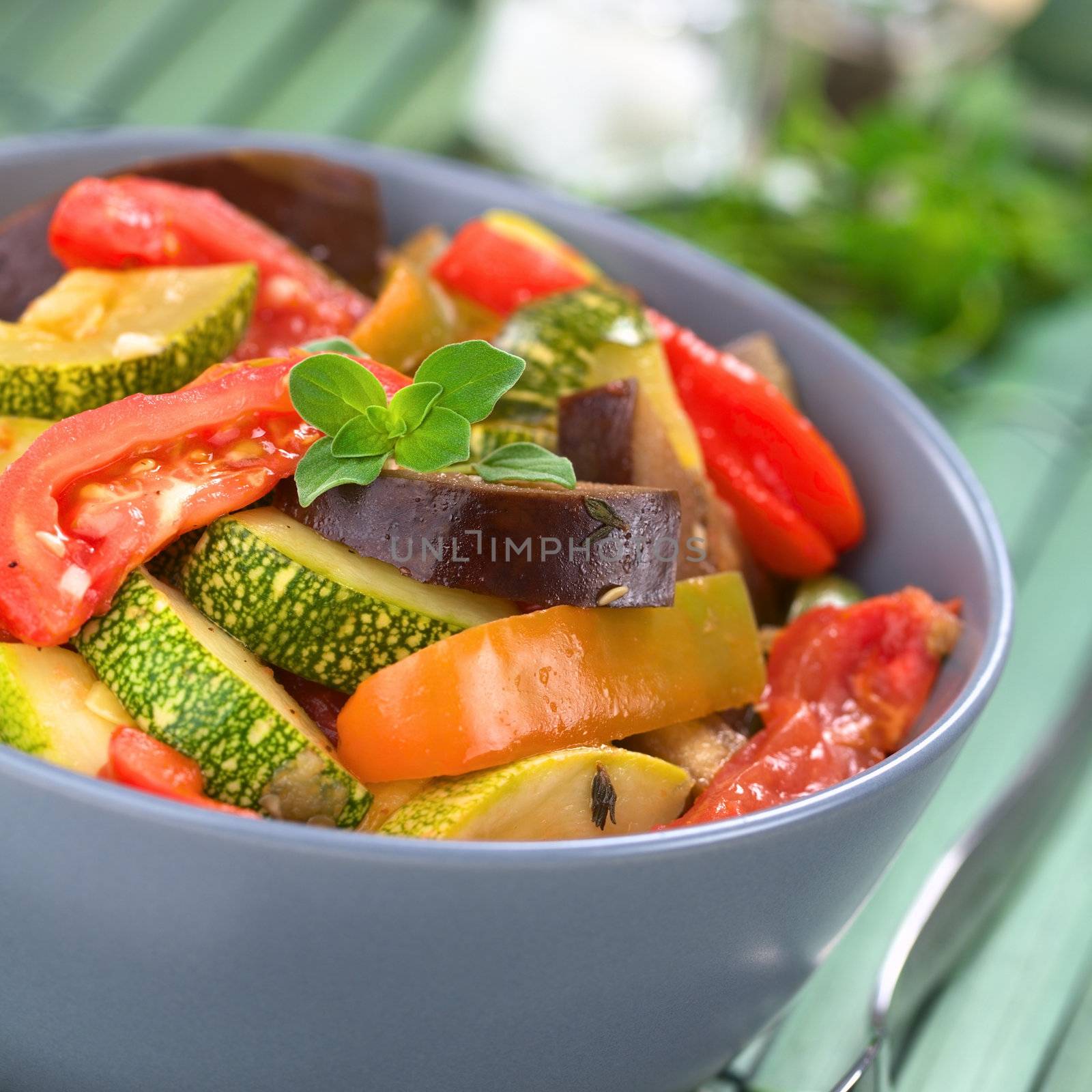 Bowl of fresh homemade Ratatouille made of eggplant, zucchini, bell pepper and tomato and seasoned with herbs (garlic, thyme, oregano), garnished with fresh oregano (Selective Focus, Focus on the oregano leaves on the meal)