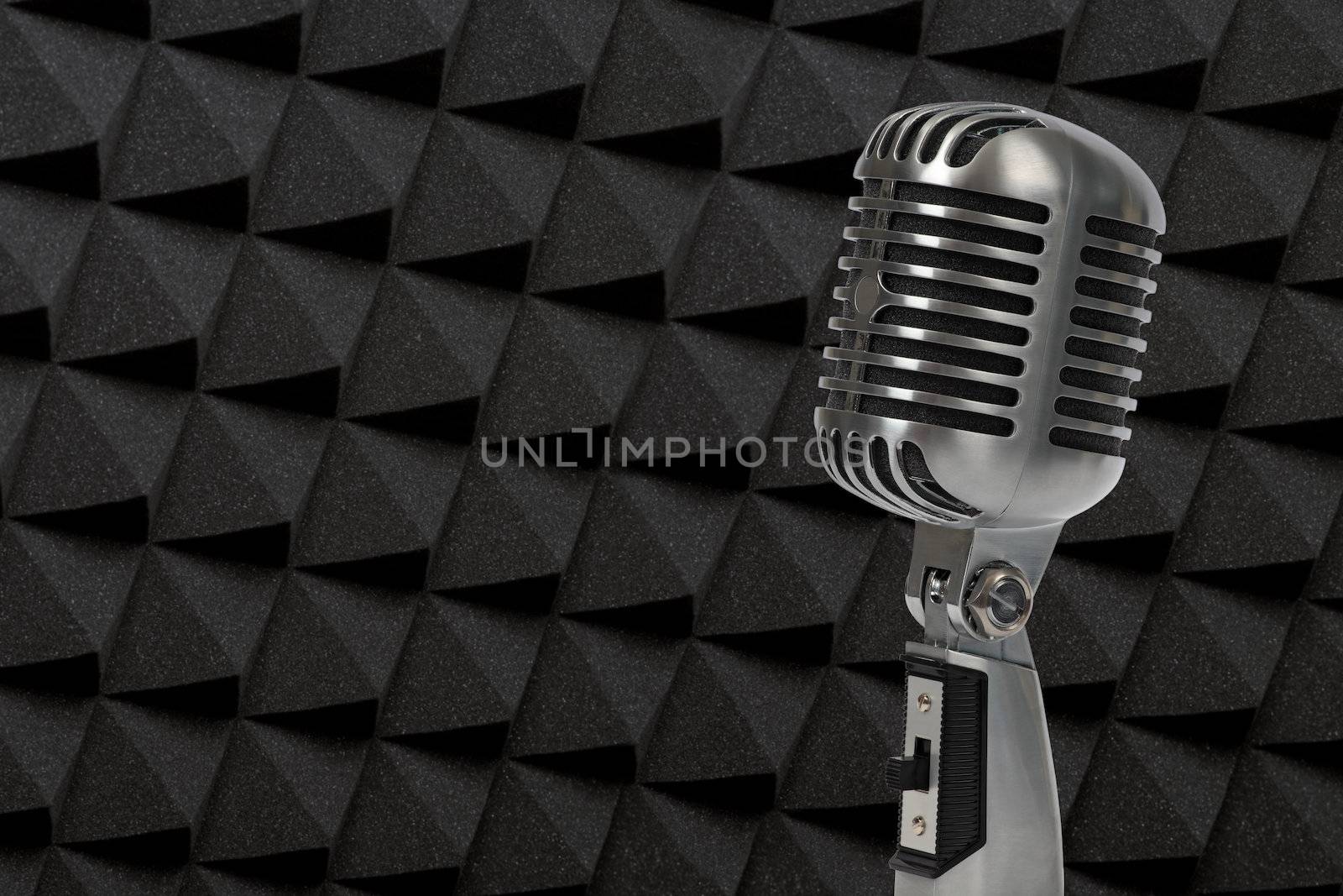 Photo of an old-fashioned microphone standing in a soundproof studio with acoustical foam on the wall.
