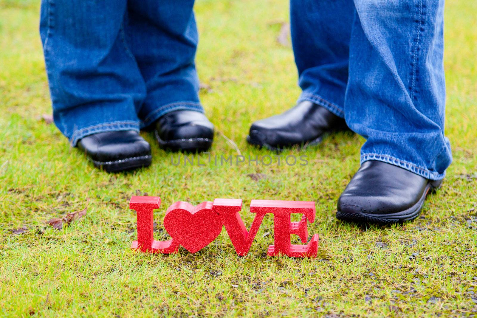The feet of a couple with the word "love" in red on the green grass.