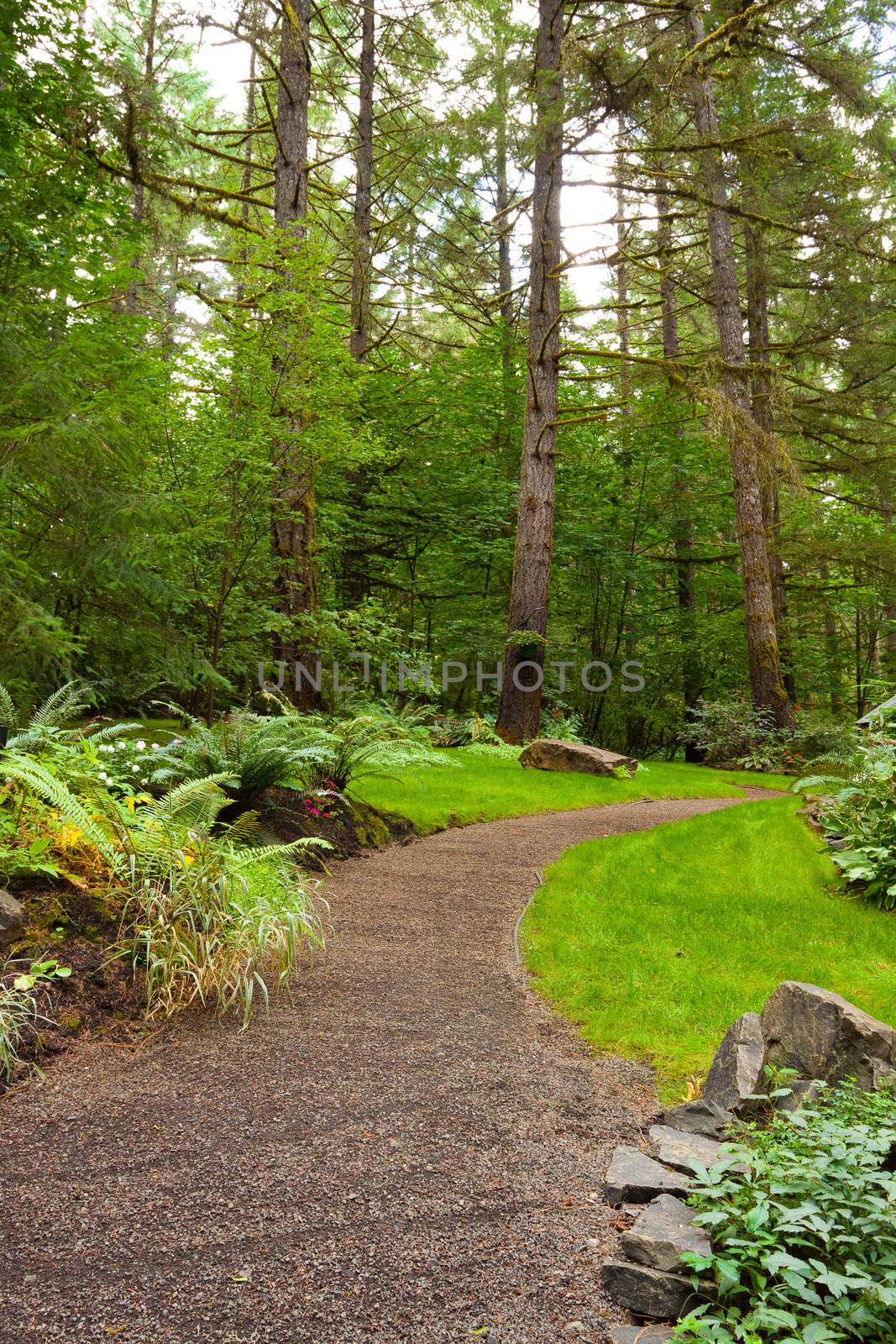 A beautiful path leads into a perfectly manicured garden at an Oregon wedding venue location. There is green, trees, plants, and stone in this vertical image.