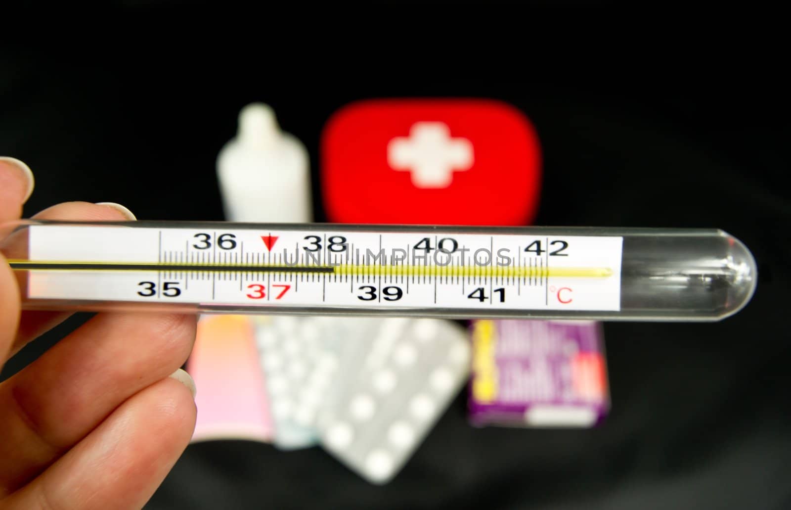 Hand holding thermometer, some of medicines in background