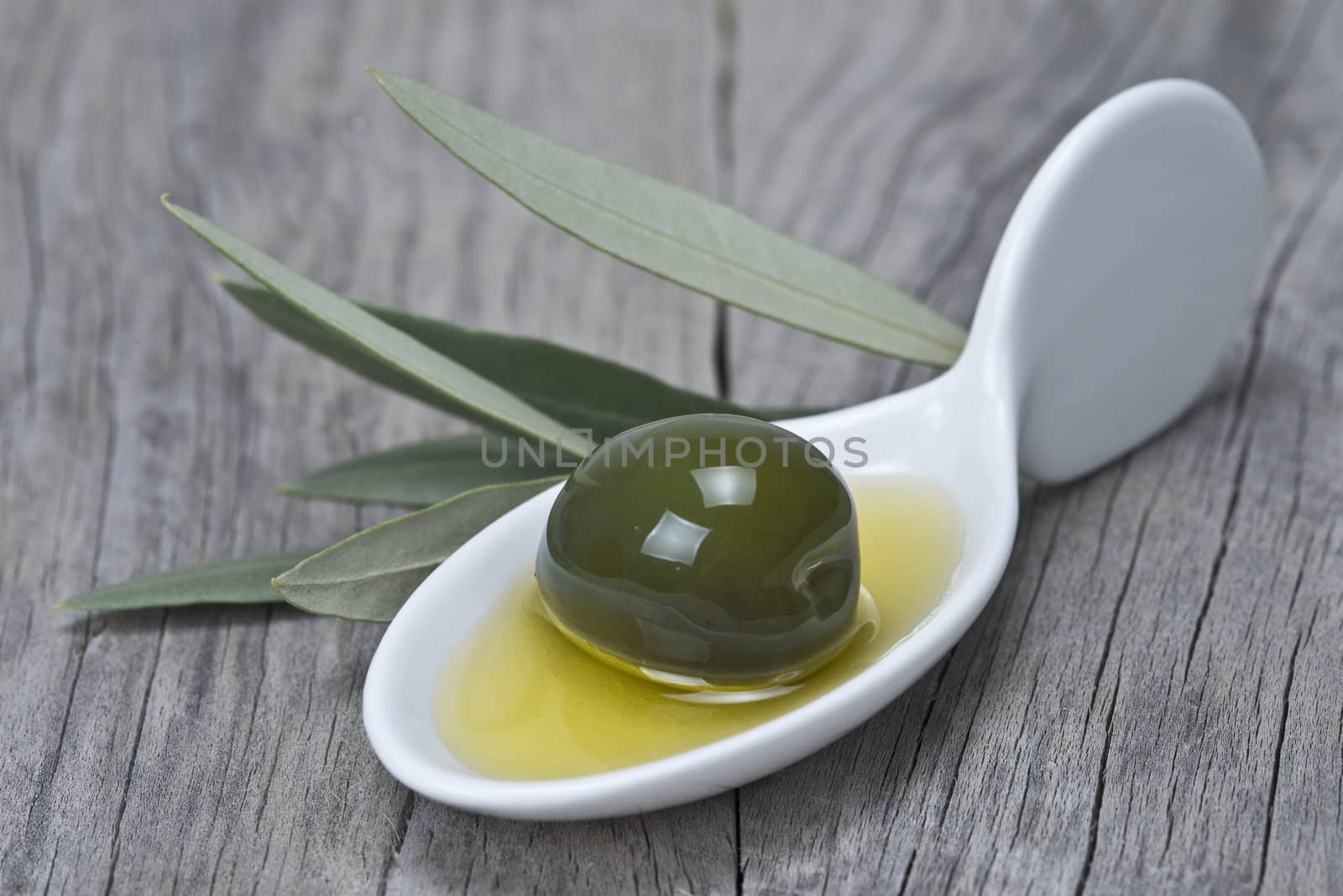 A china spoon with olives and leaves on a wooden surface
