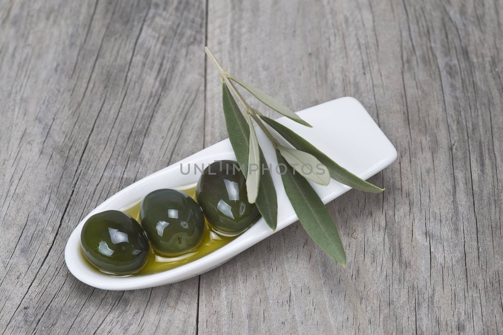 A china spoon with olives and leaves on a wooden surface
