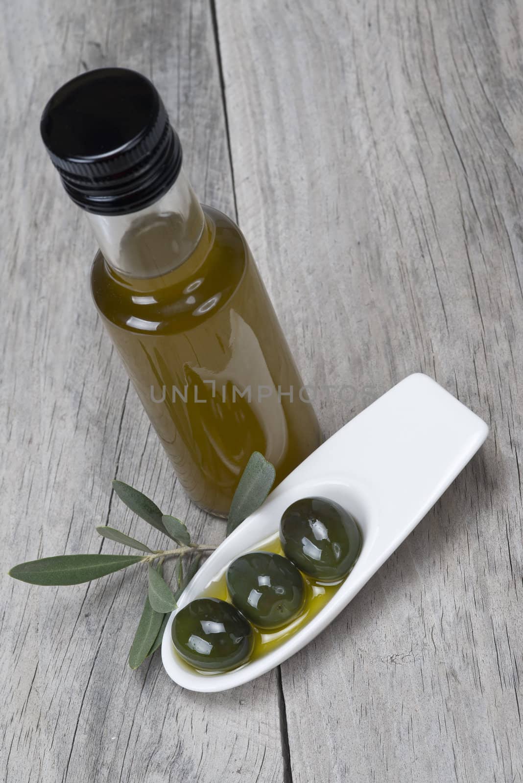 Olive oil bottle and some olives in a china spoon on a wooden surface