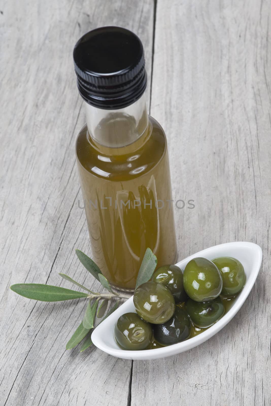 Olive oil bottle and some olives in a china spoon on a wooden surface