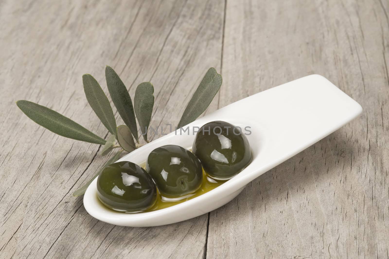 A china spoon with olives and leaves on a wooden surface
