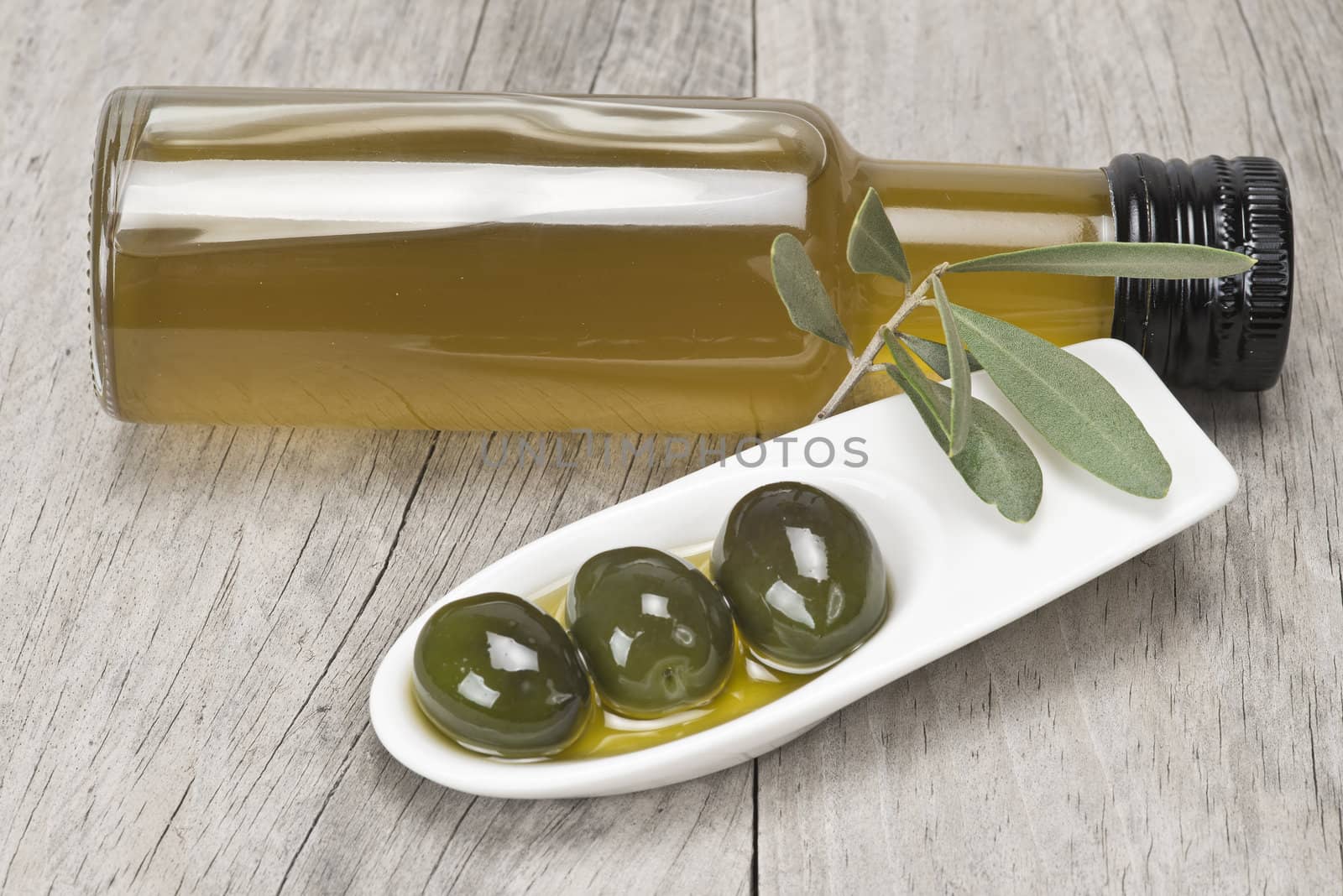 Olive oil bottle and some olives in a china spoon on a wooden surface