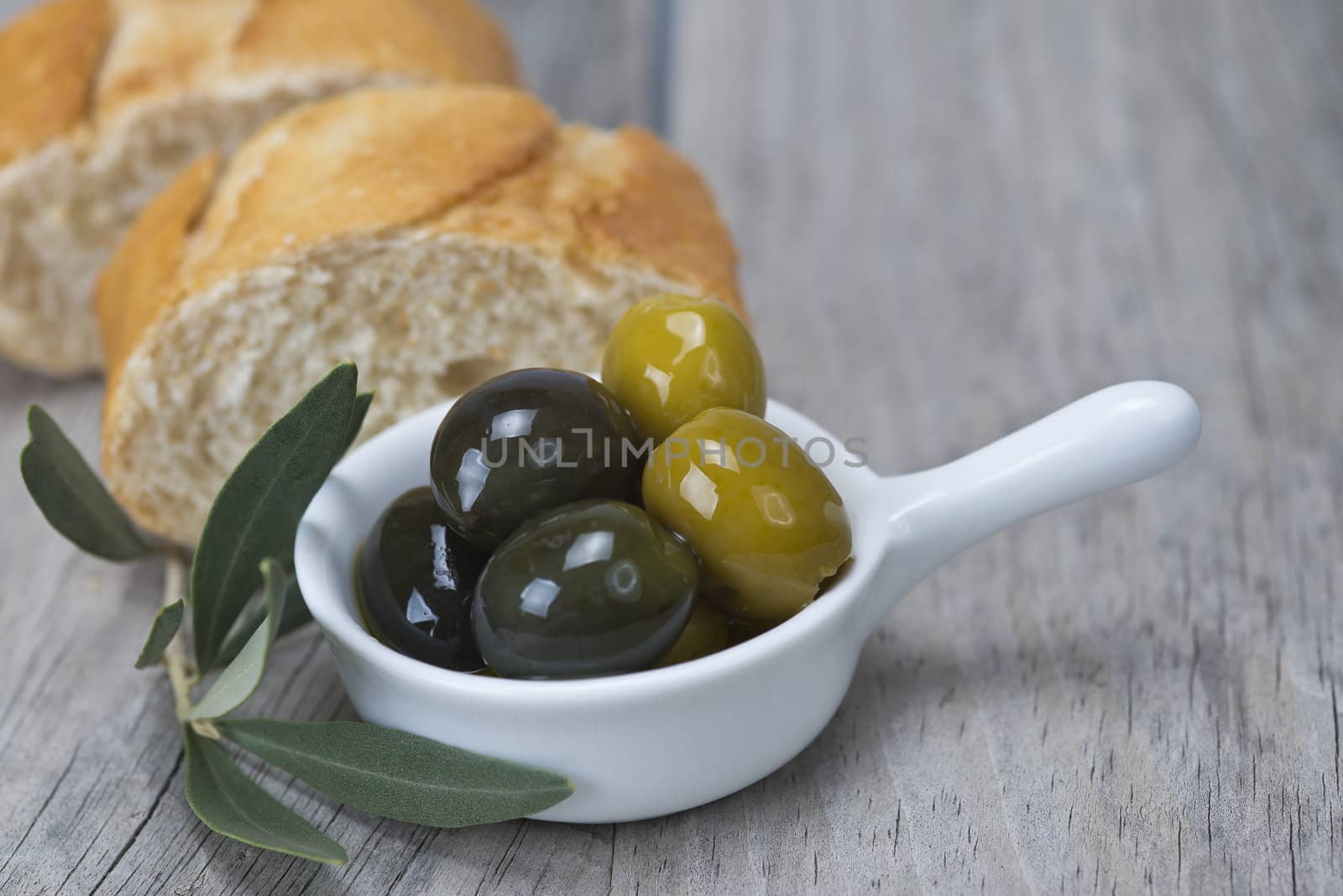 Olive oil with green olives and bread on a wooden surface