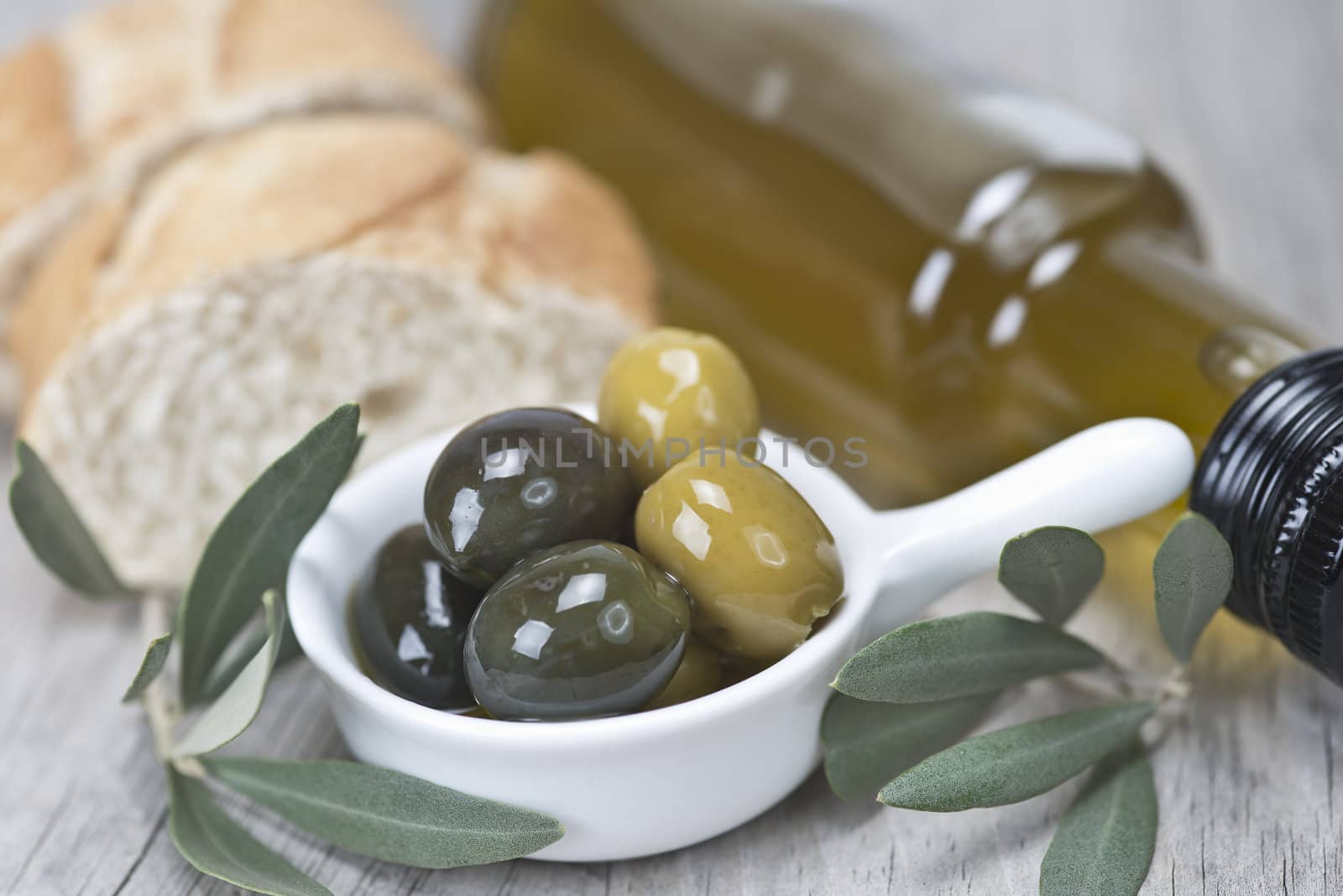 Olive oil with green olives and bread on a wooden surface