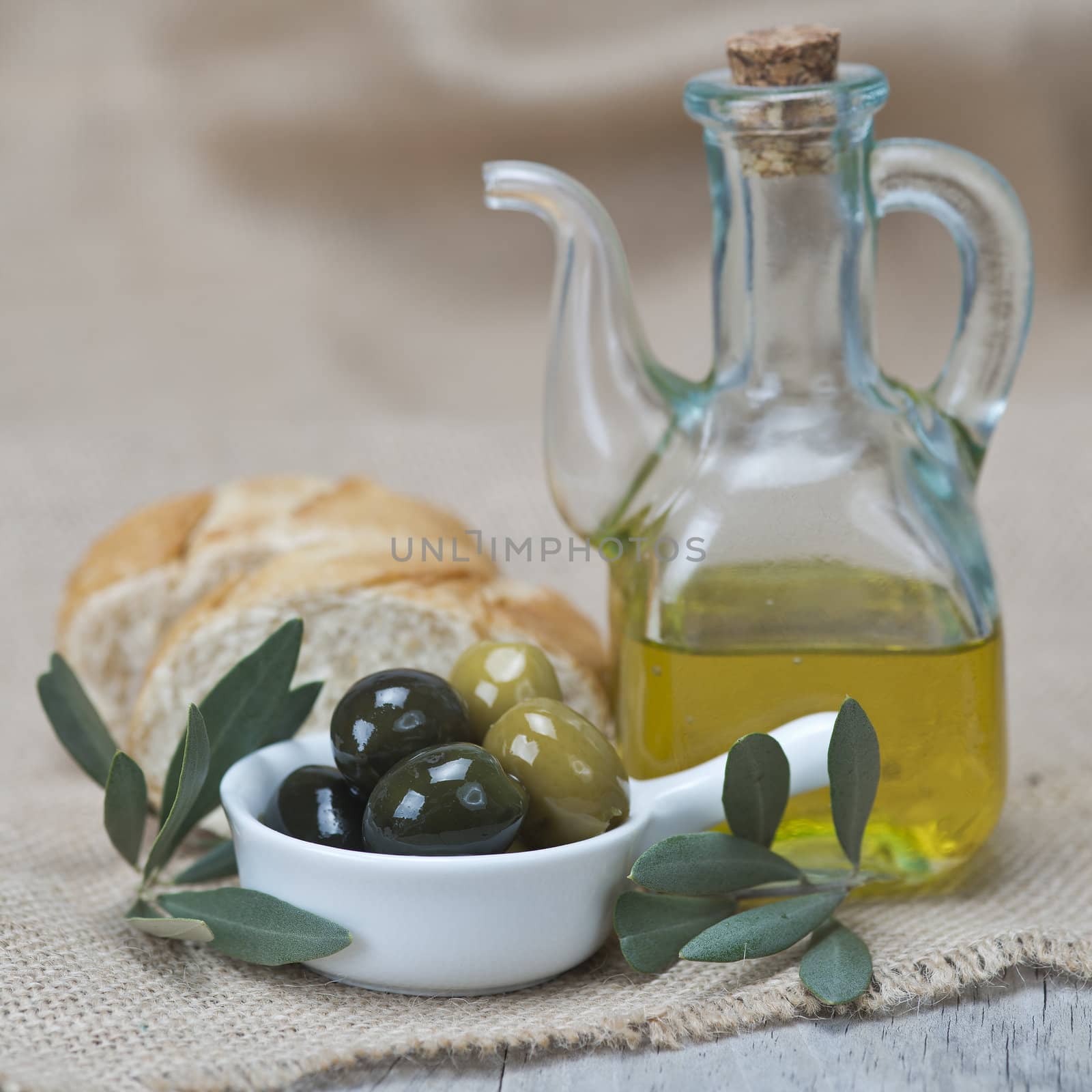 Olive oil with green olives and bread on a wooden surface