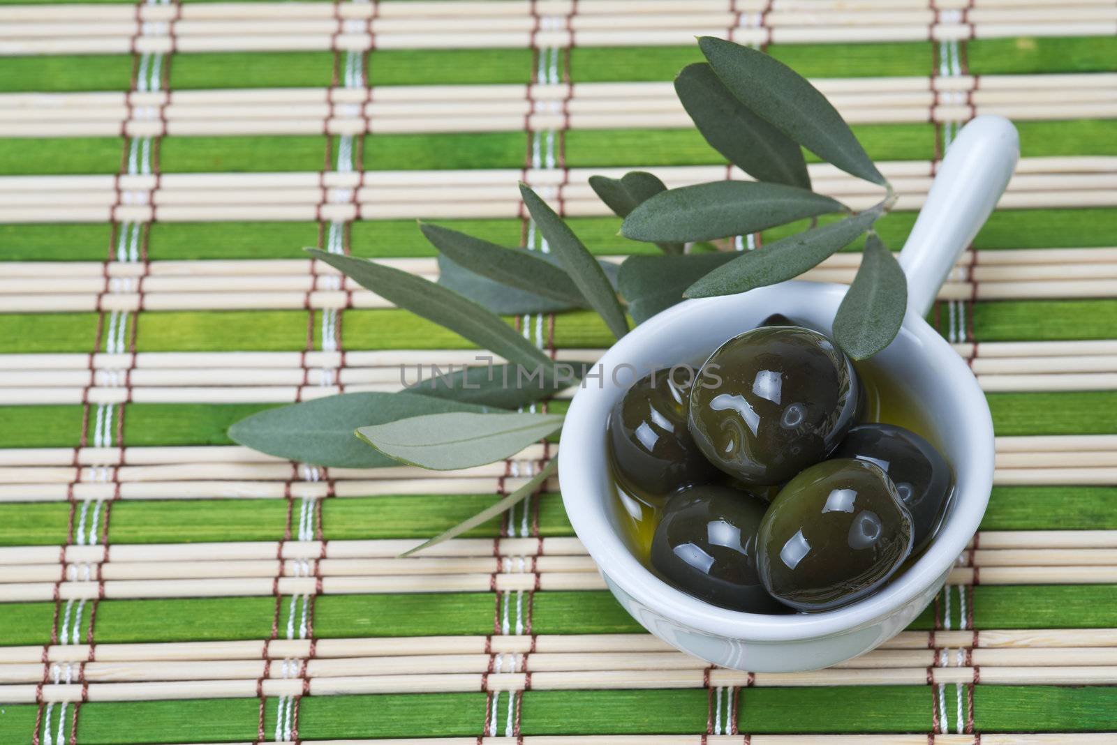 China spoon with olives a its leaves on a bamboo mat