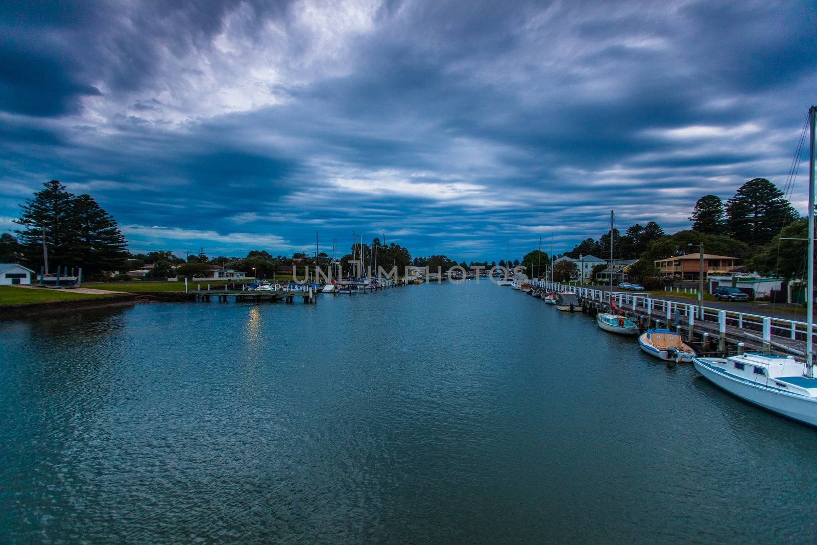 View from evening footbridge walkway across Moyne River in Port Fairy, VIC. Calm water with dramatic cloud overhead.