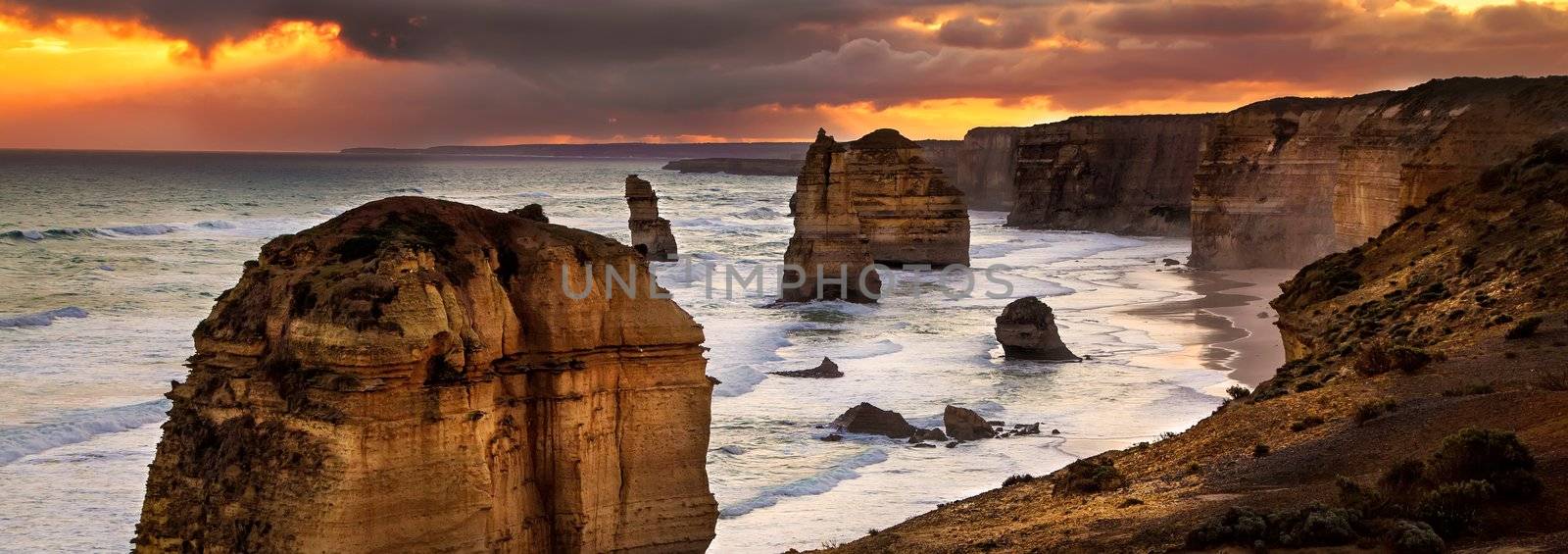 Golden sunset at 12 Apostles rock formation in Victoria, Australia. Dusk sun setting behind the backlit apostles with sea fog rolling in to the cliff face.
