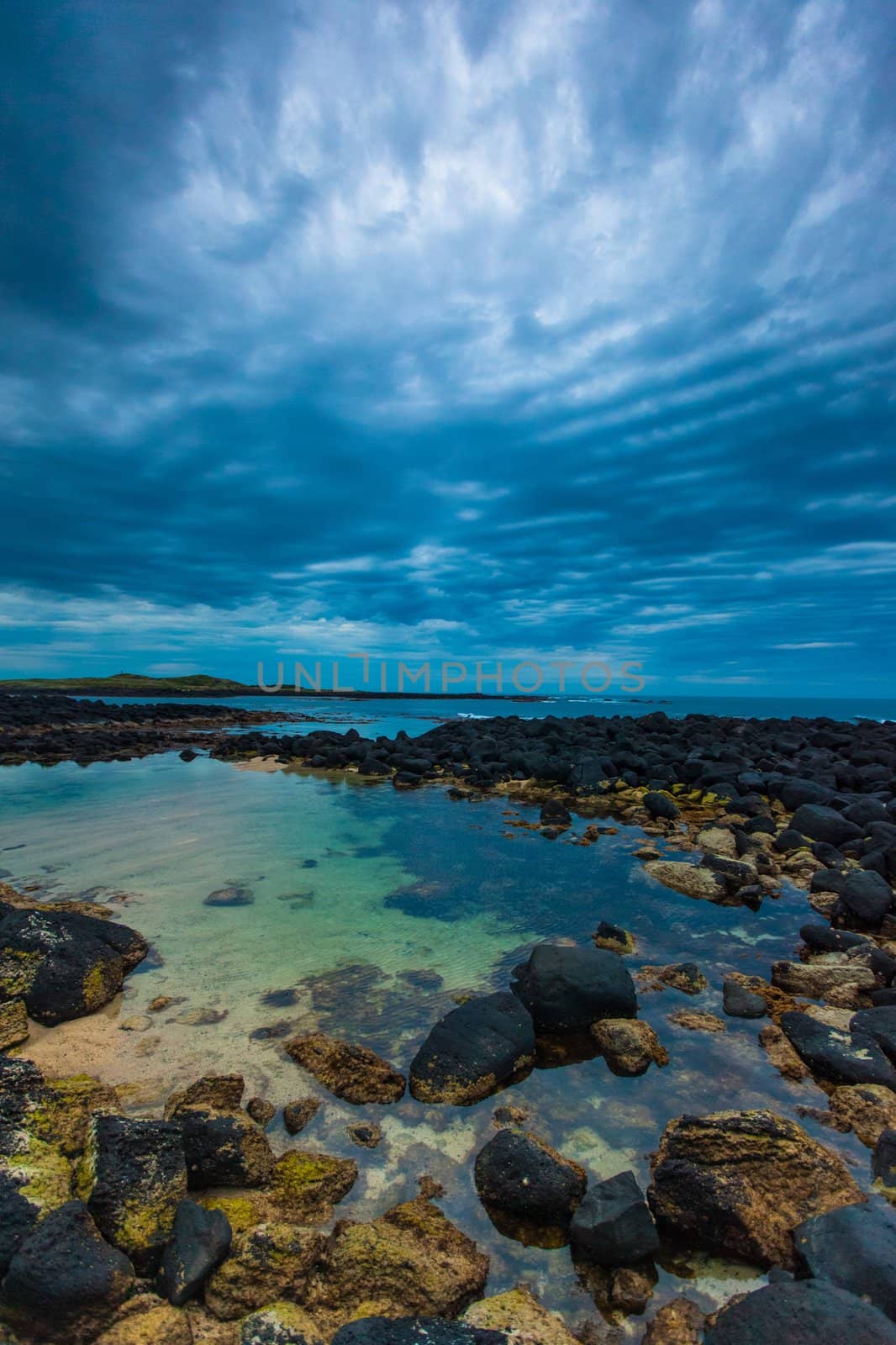 Dusk (Sunset) over black volcanic rocky tidal pool and sky full of rolling cloud in Port Fairy, Victoria, Australia.