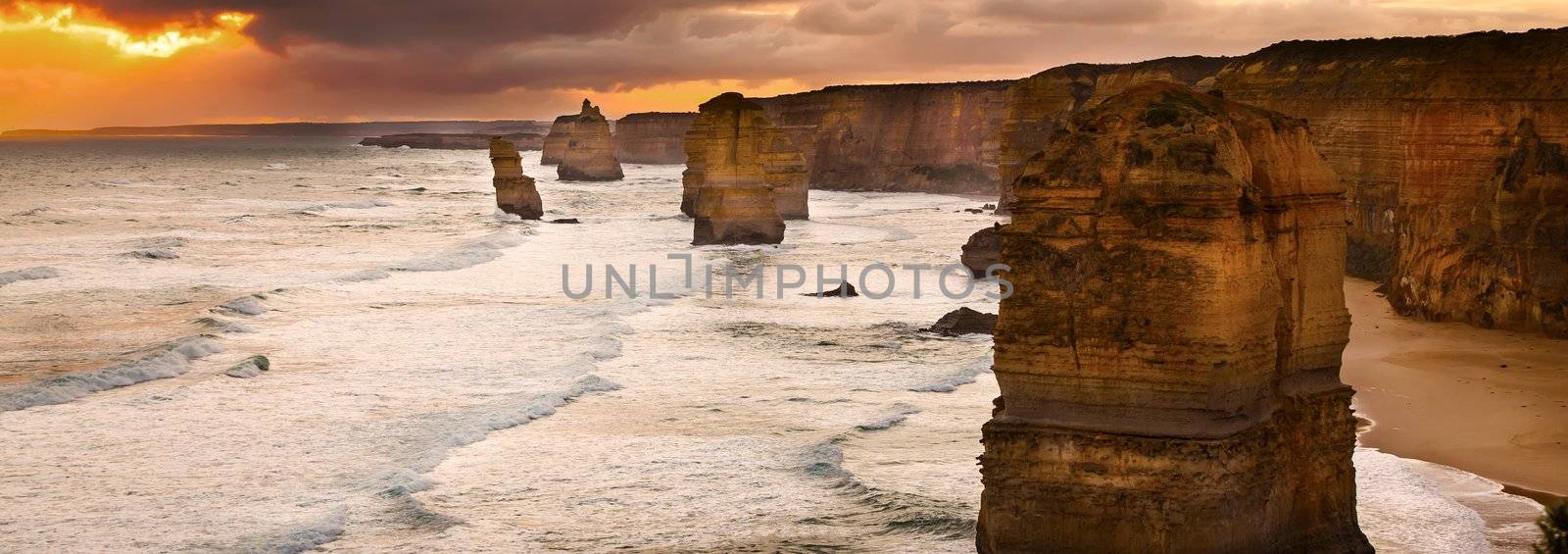 Golden sunset at 12 Apostles rock formation in Victoria, Australia. Dusk sun setting behind the backlit apostles with sea fog rolling in to the cliff face.