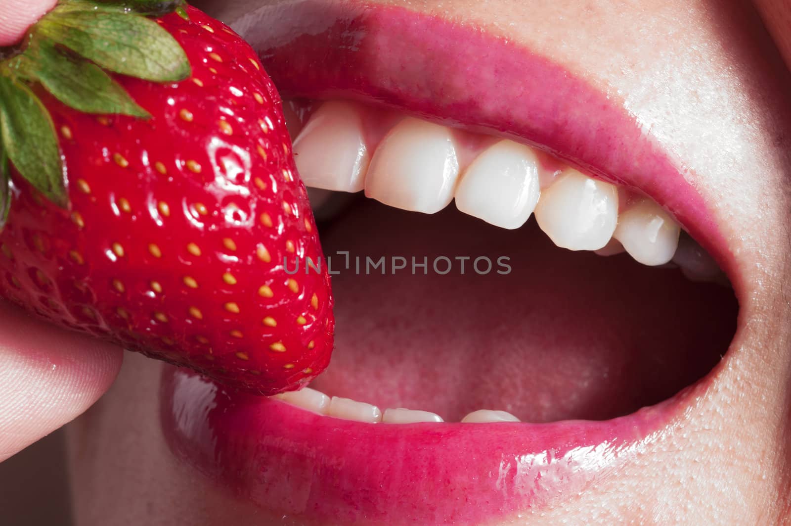 Macro close up of a beautiful female mouth eating a fresh strawberry by TanawatPontchour