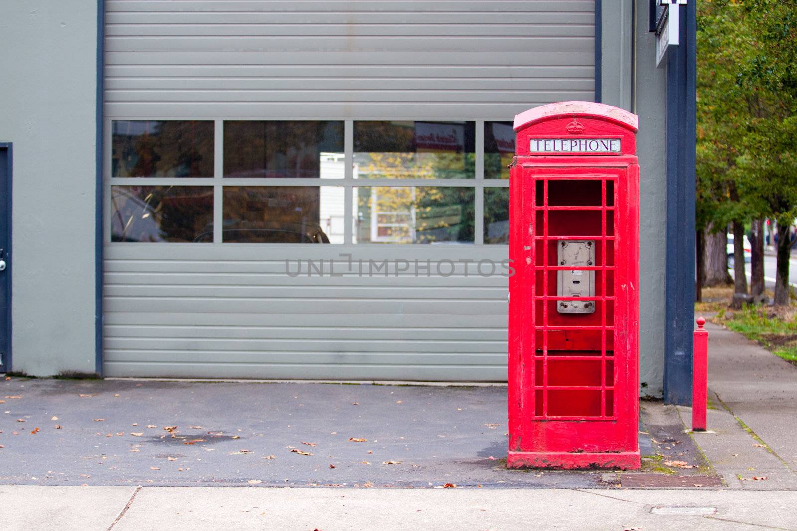 A bright red telephone booth sits abandoned on a street corner.