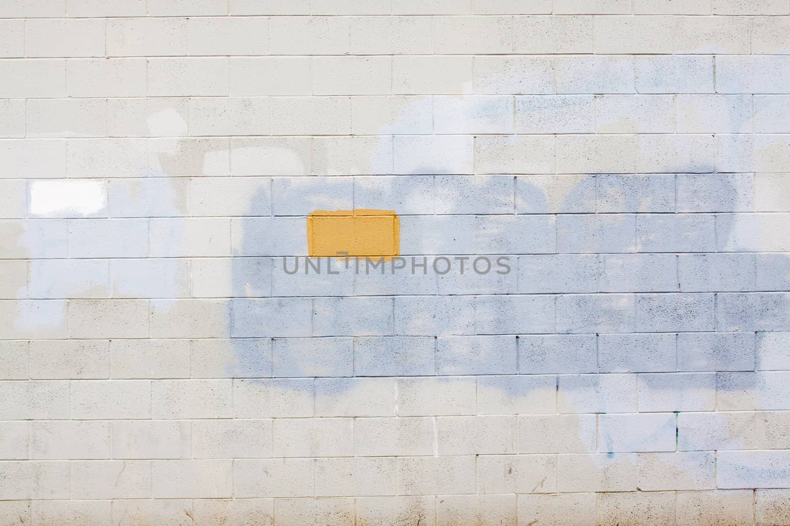 A grey wall has rectangular and square patches of paint used to cover up graffiti and vandalism along the side of an urban building.