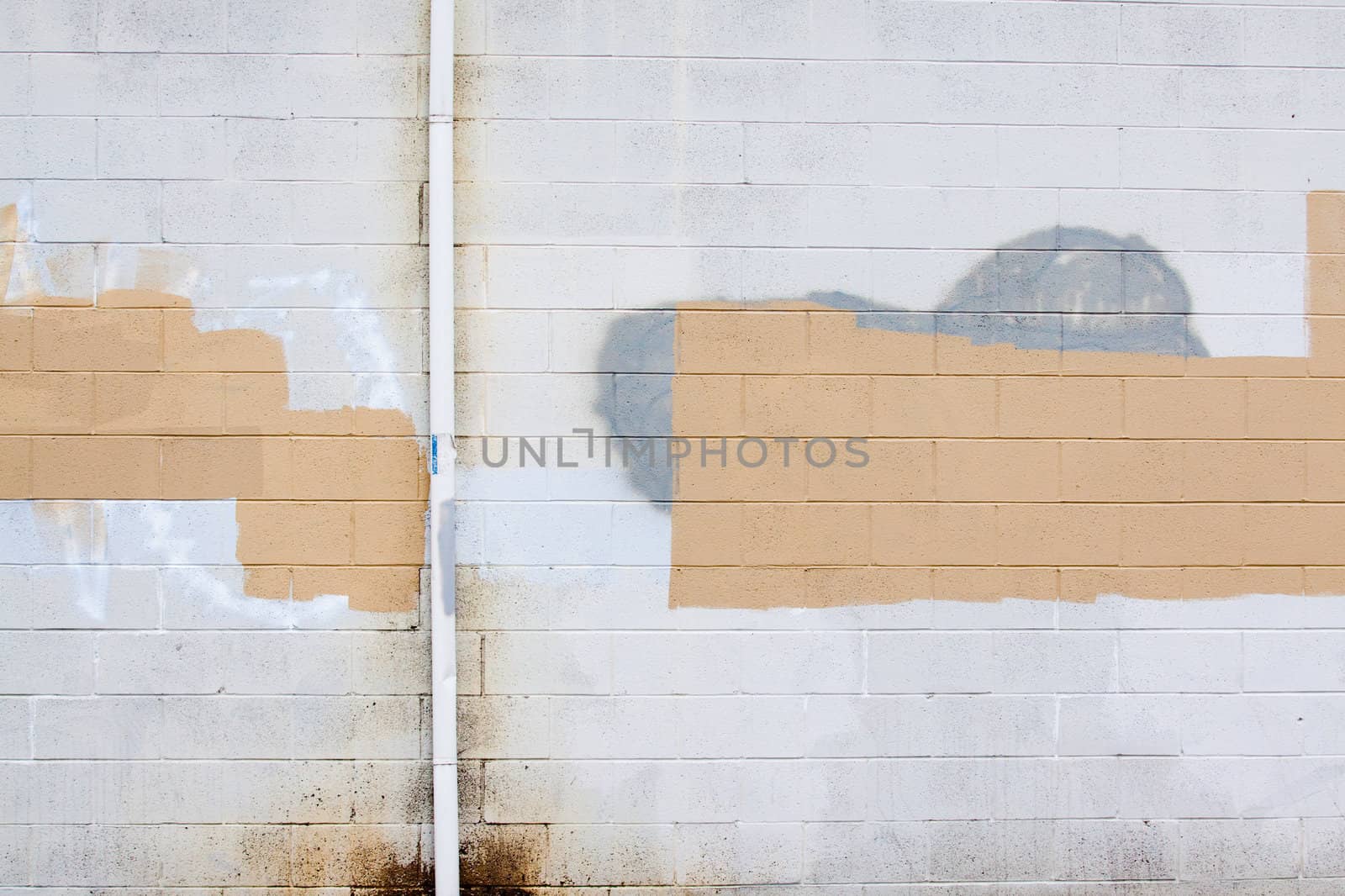 A grey wall has rectangular and square patches of paint used to cover up graffiti and vandalism along the side of an urban building.