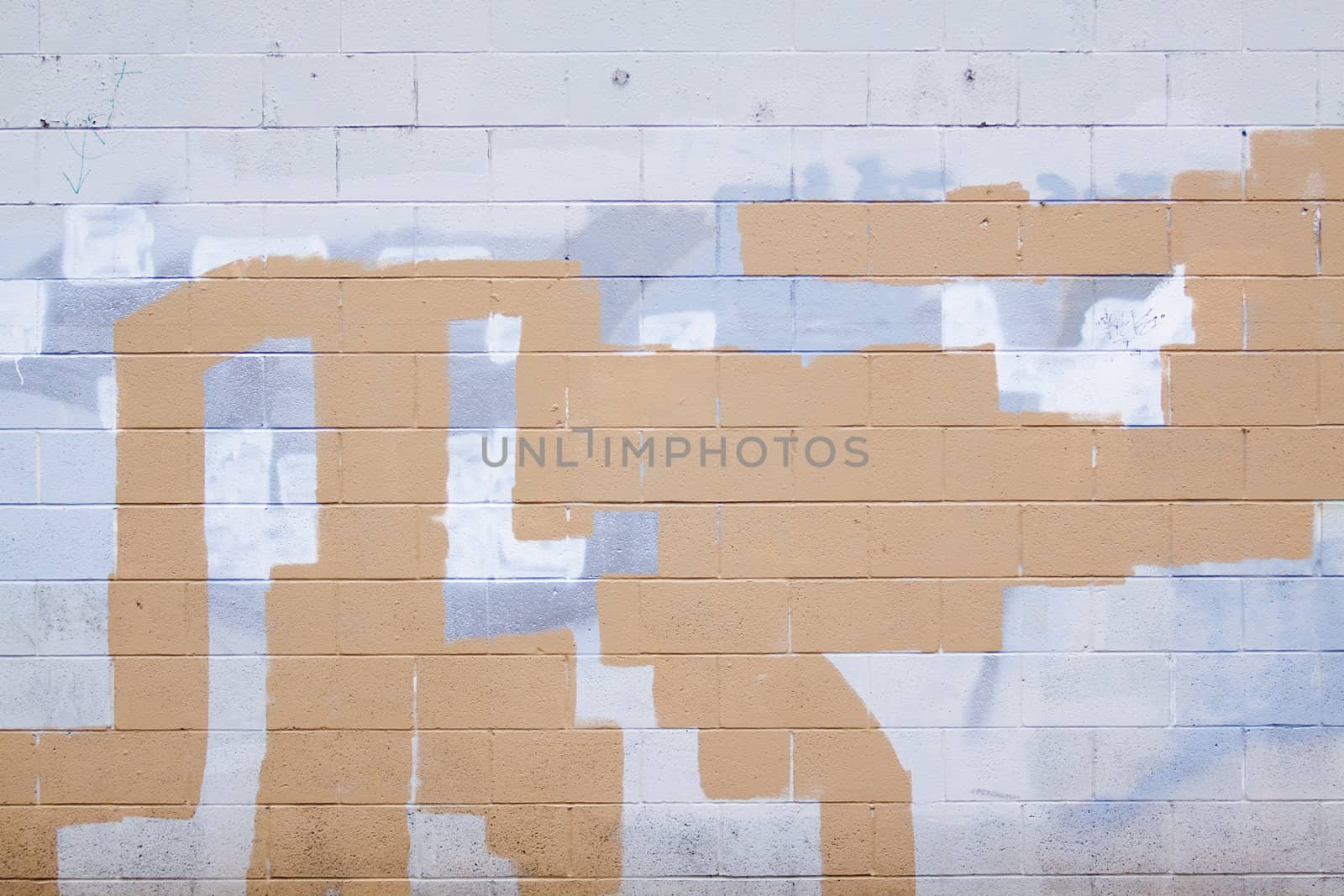 A grey wall has rectangular and square patches of paint used to cover up graffiti and vandalism along the side of an urban building.