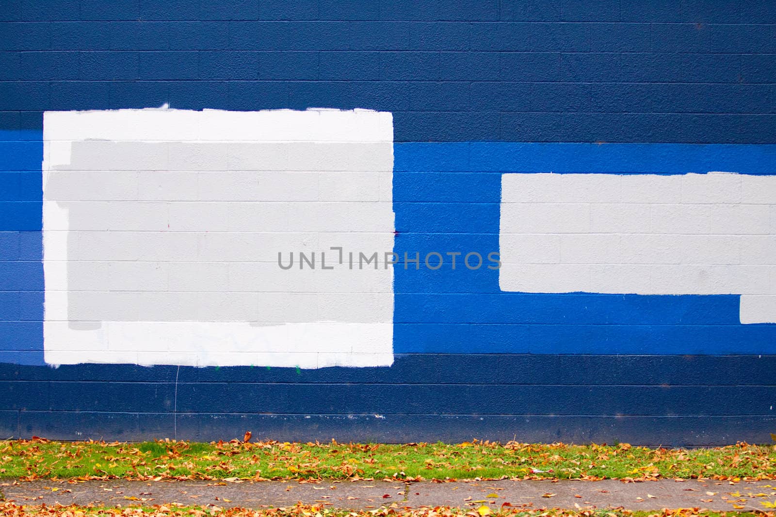 A dark blue wall of a building next to a street with autumn leaves during the fall that has grey rectangles of paint to cover up graffiti.