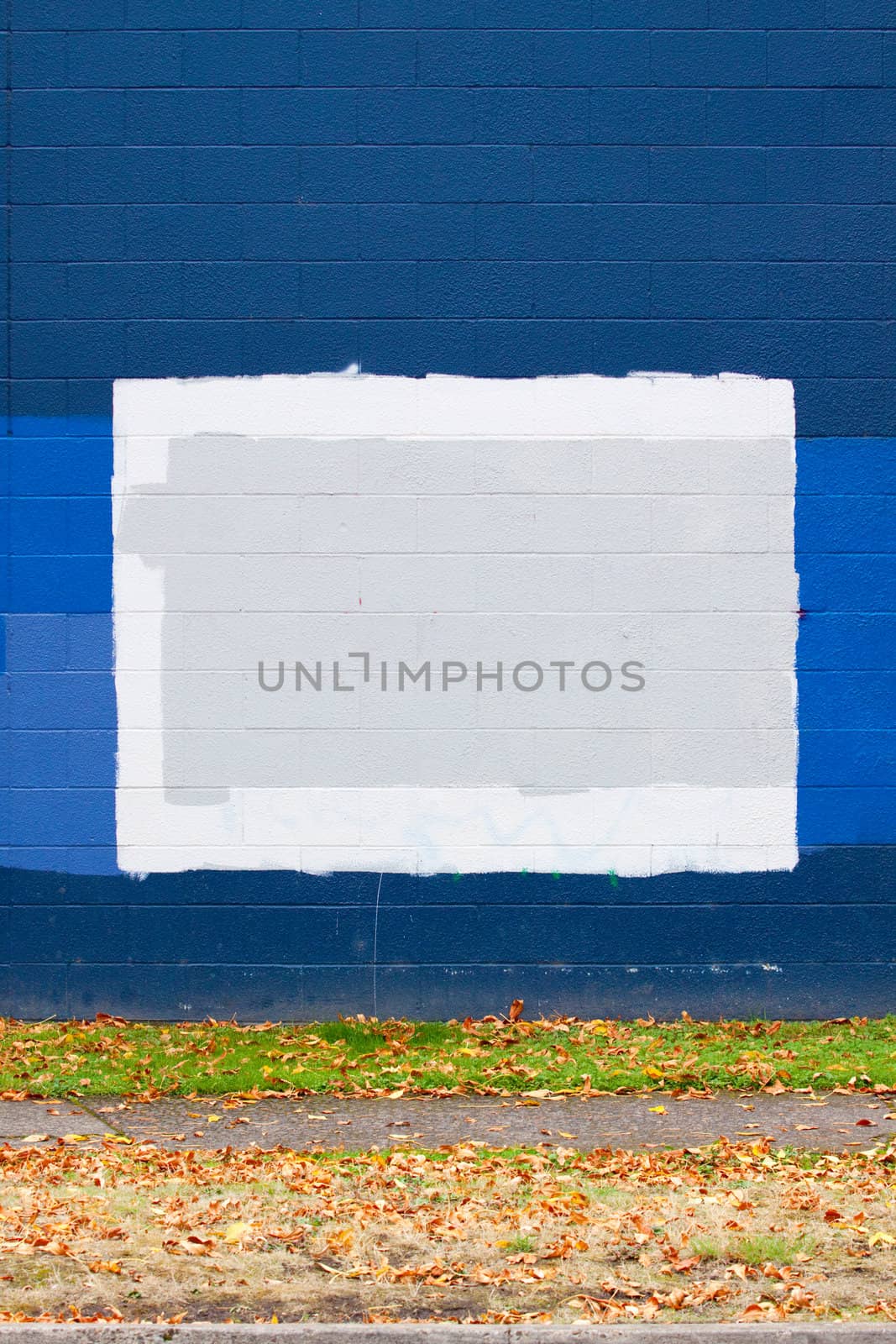 A dark blue wall of a building next to a street with autumn leaves during the fall that has grey rectangles of paint to cover up graffiti.