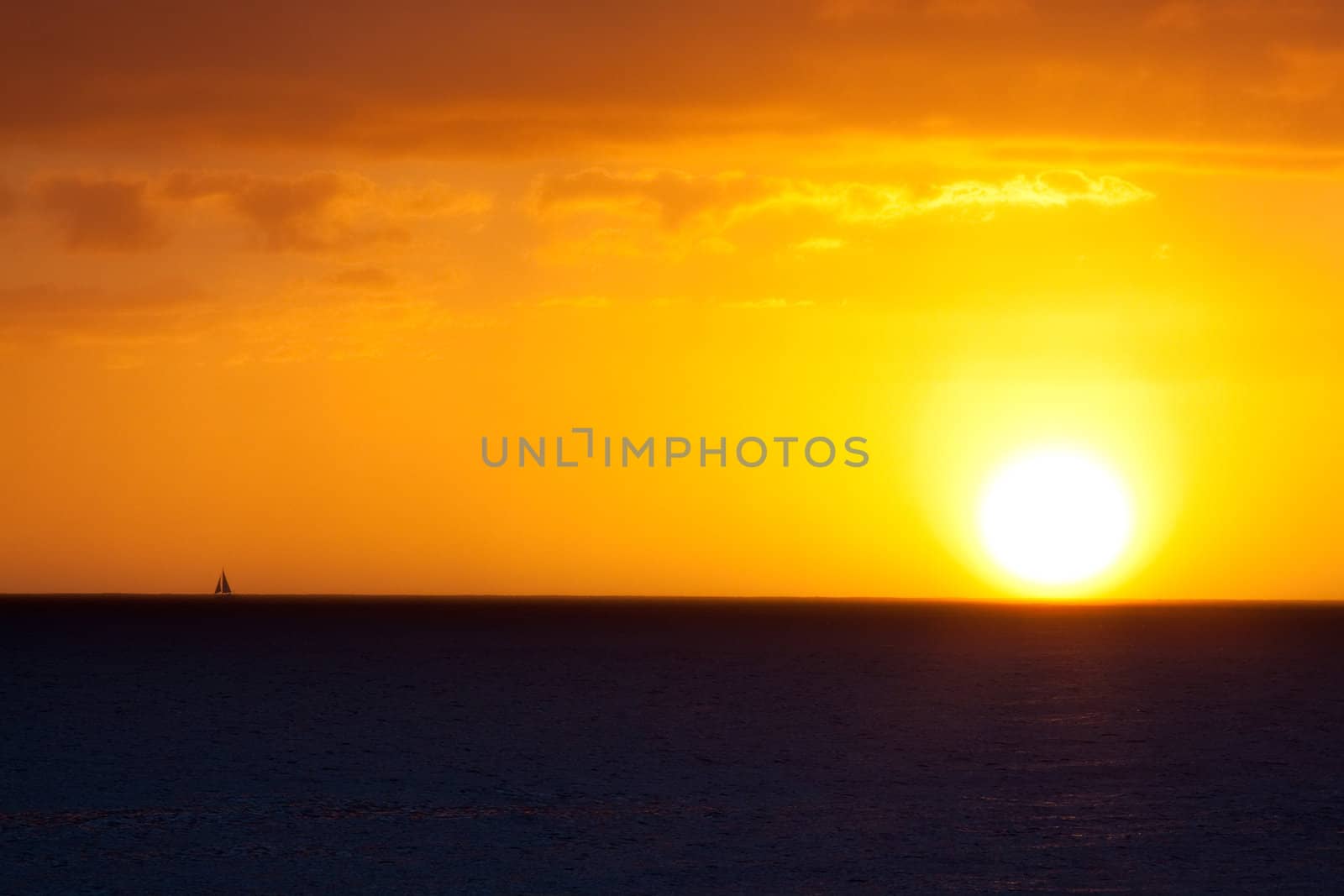 A sailboat sails offshore during a sunset in Oahu Hawaii along the north shore.