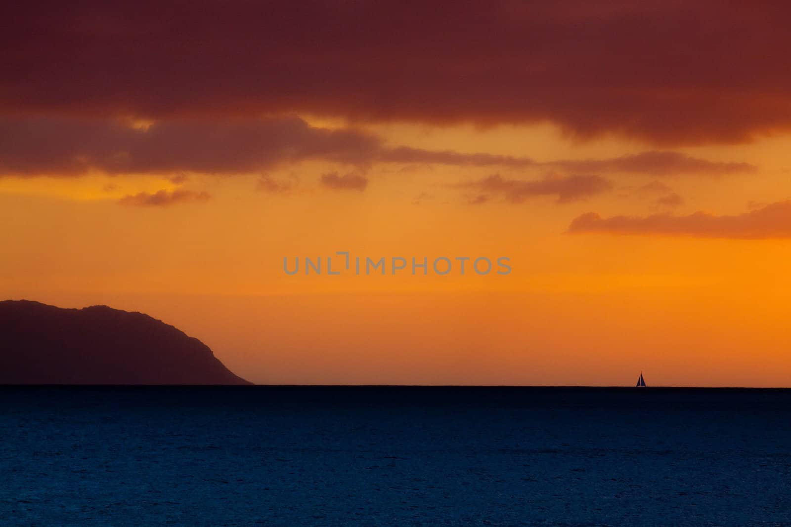 A sailboat sails offshore during a sunset in Oahu Hawaii along the north shore.