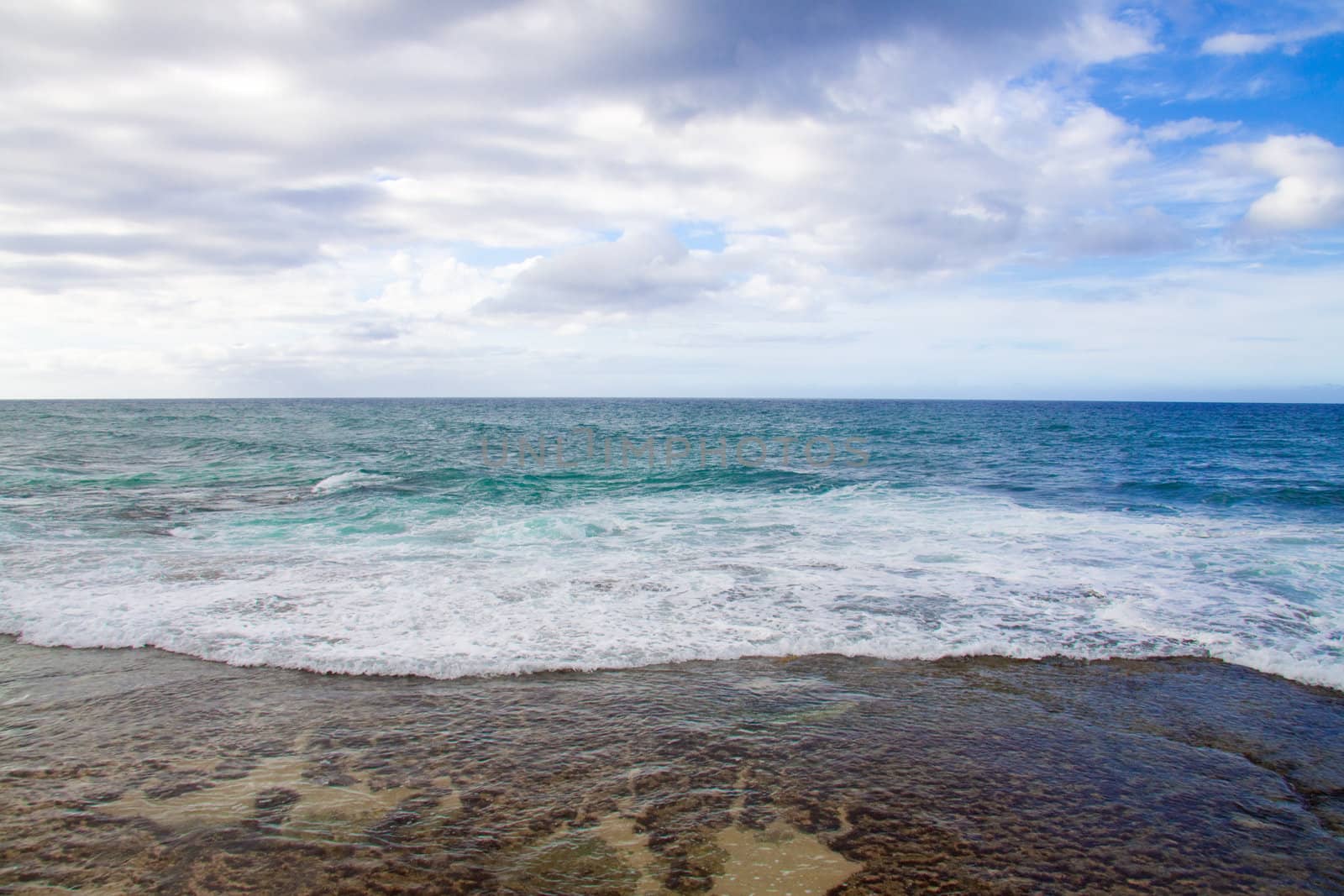 A beautiful beach with nobody in the scene as well as a dynamic sky and nice turquoise and blue tones throughout in color.