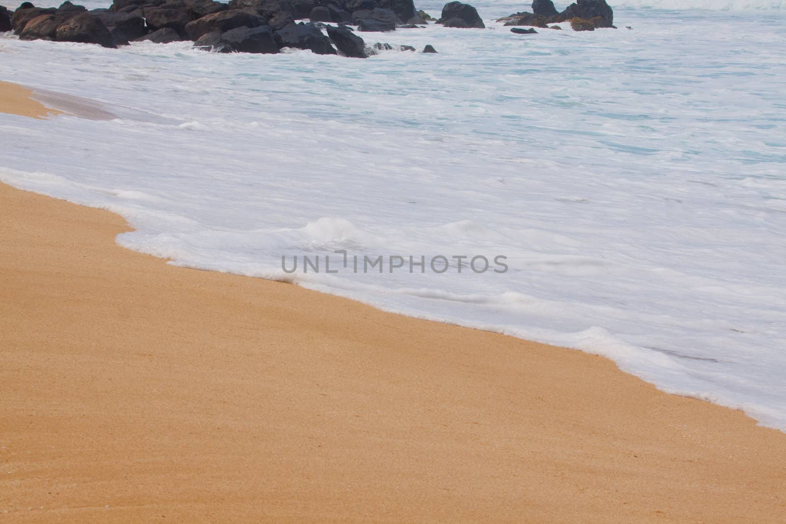 White surf water comes onto the beach in a frothy substance on the north shore of oahu hawaii.