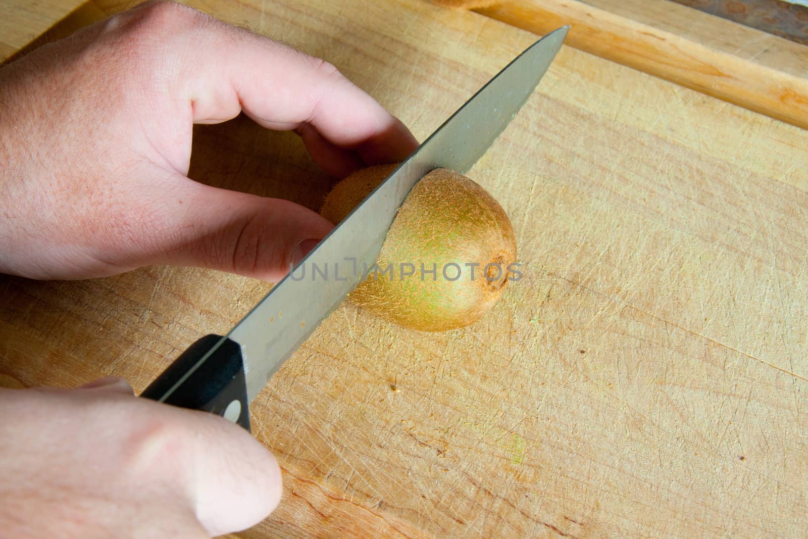 A man slices a kiwi fruit on a cutting board to prepare a breakfast meal.