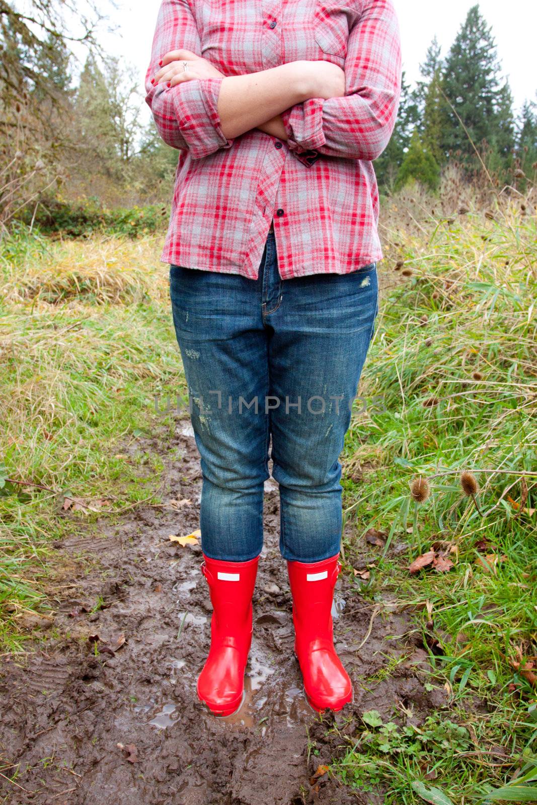Bright shining clean red rain boots on a girl while she stands in the mud puddle.