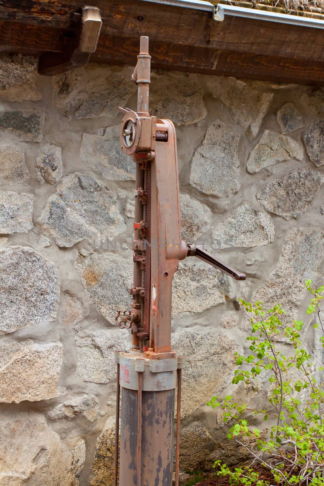 A pump for an old well is rusted and weathered outside a vintage home.