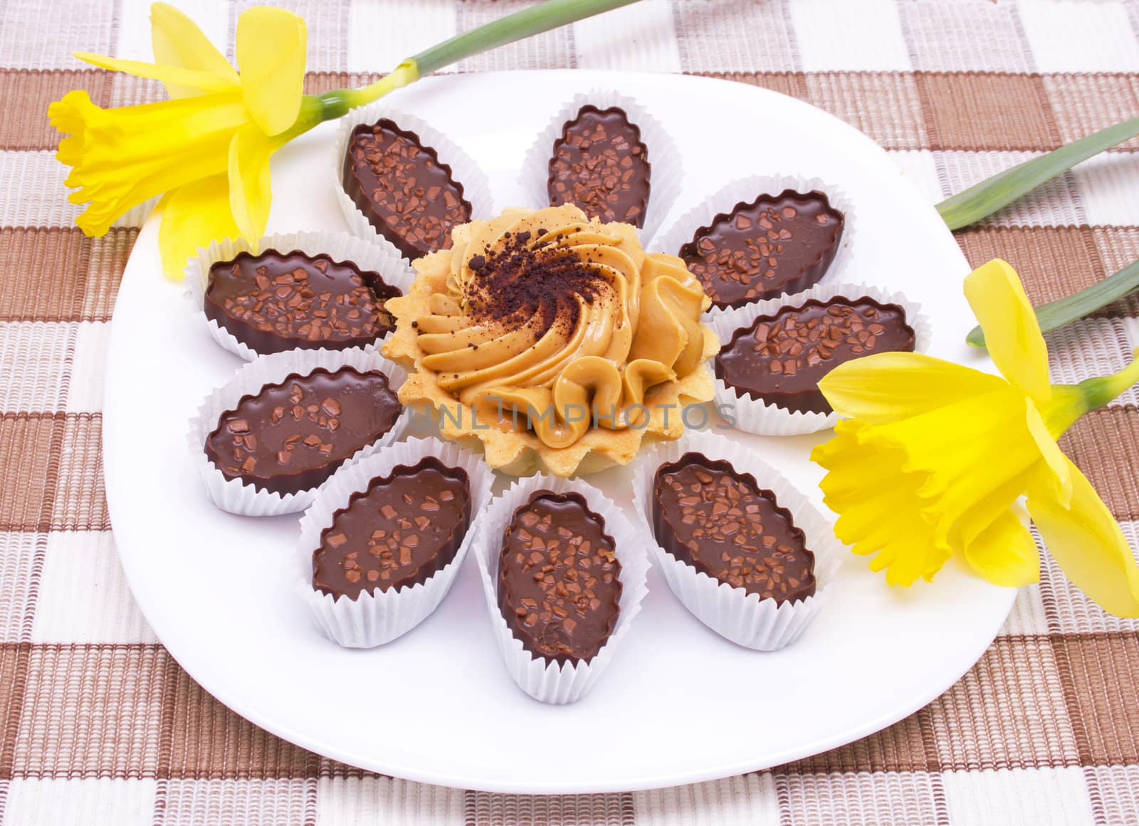 Cake and chocolates on the white plate with two yellow daffodils