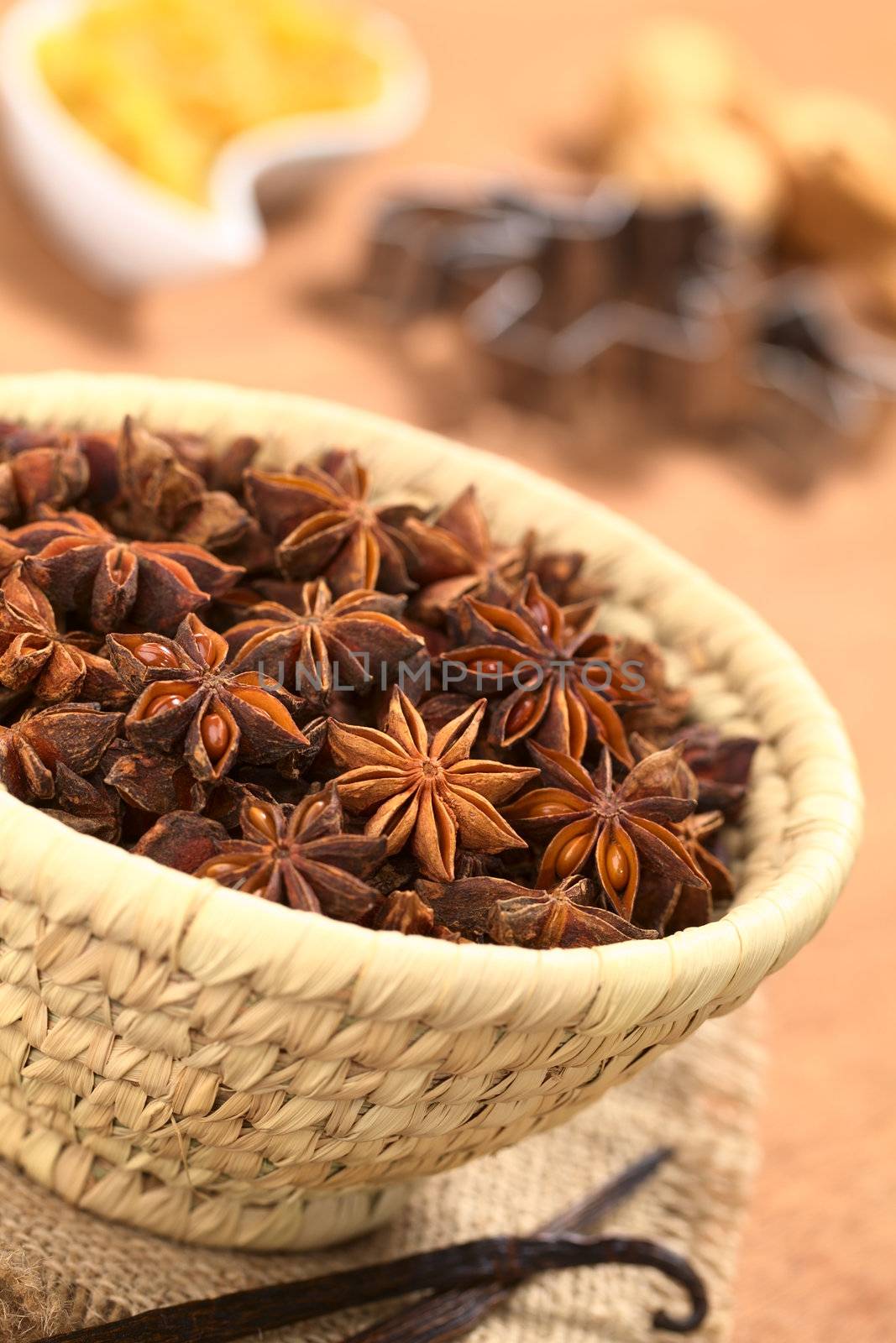 Star anise in small woven basket with vanilla in front and other baking ingredients in the back (Selective Focus, Focus one third into the anise)