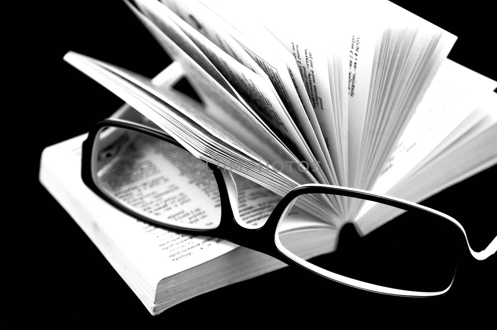 Small open book and glasses on it, isolated on black background