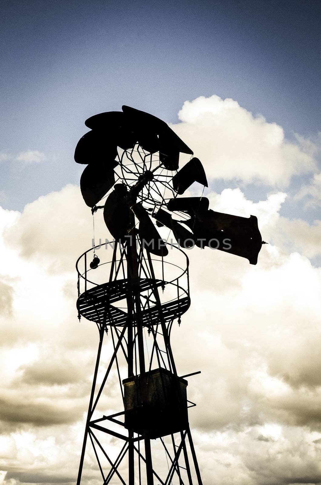 Old Farm Windmill for Pumping Water with Spinning Blades against cloudy sky.