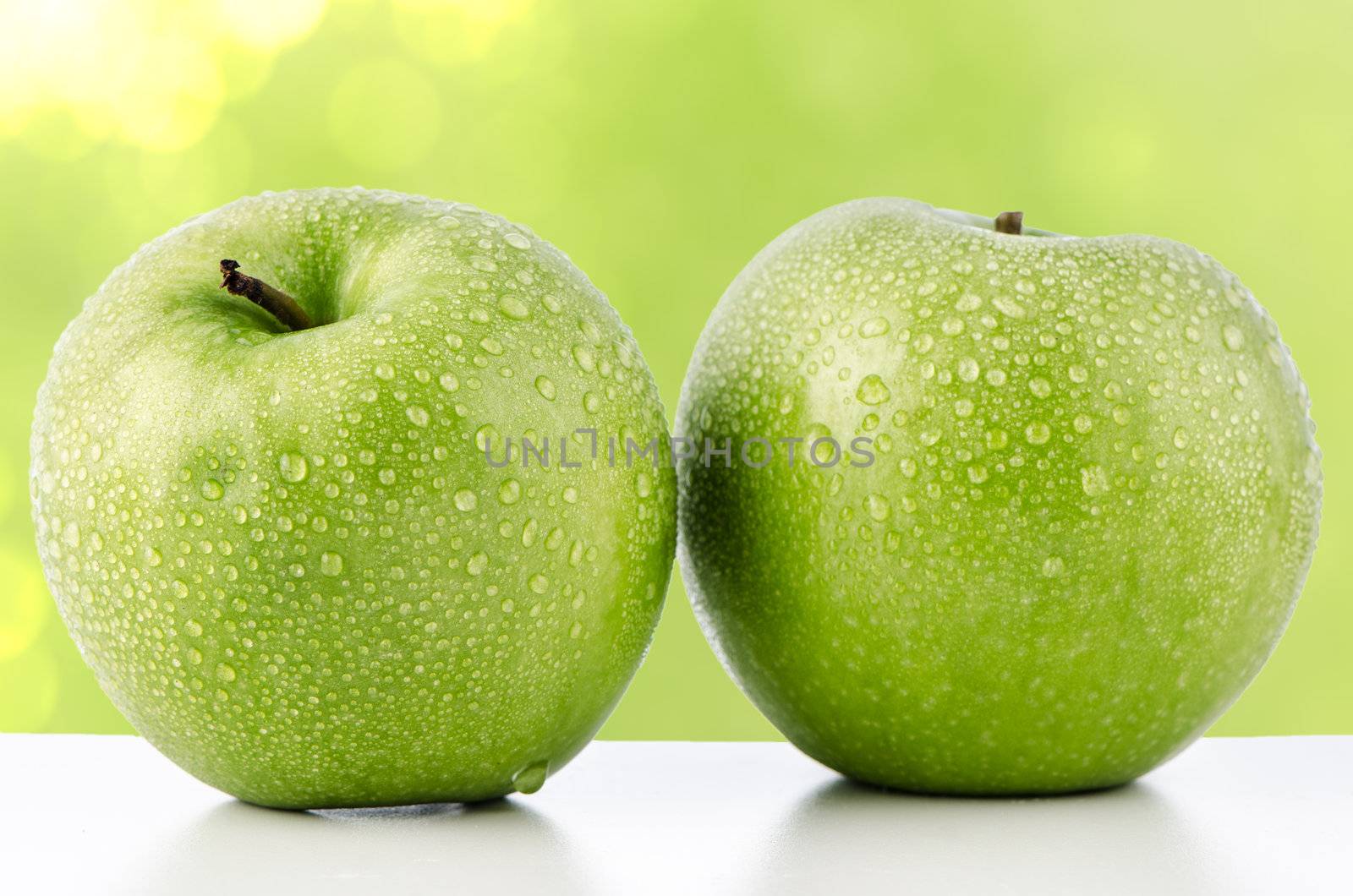 Two fresh green apples on green defocused background.
