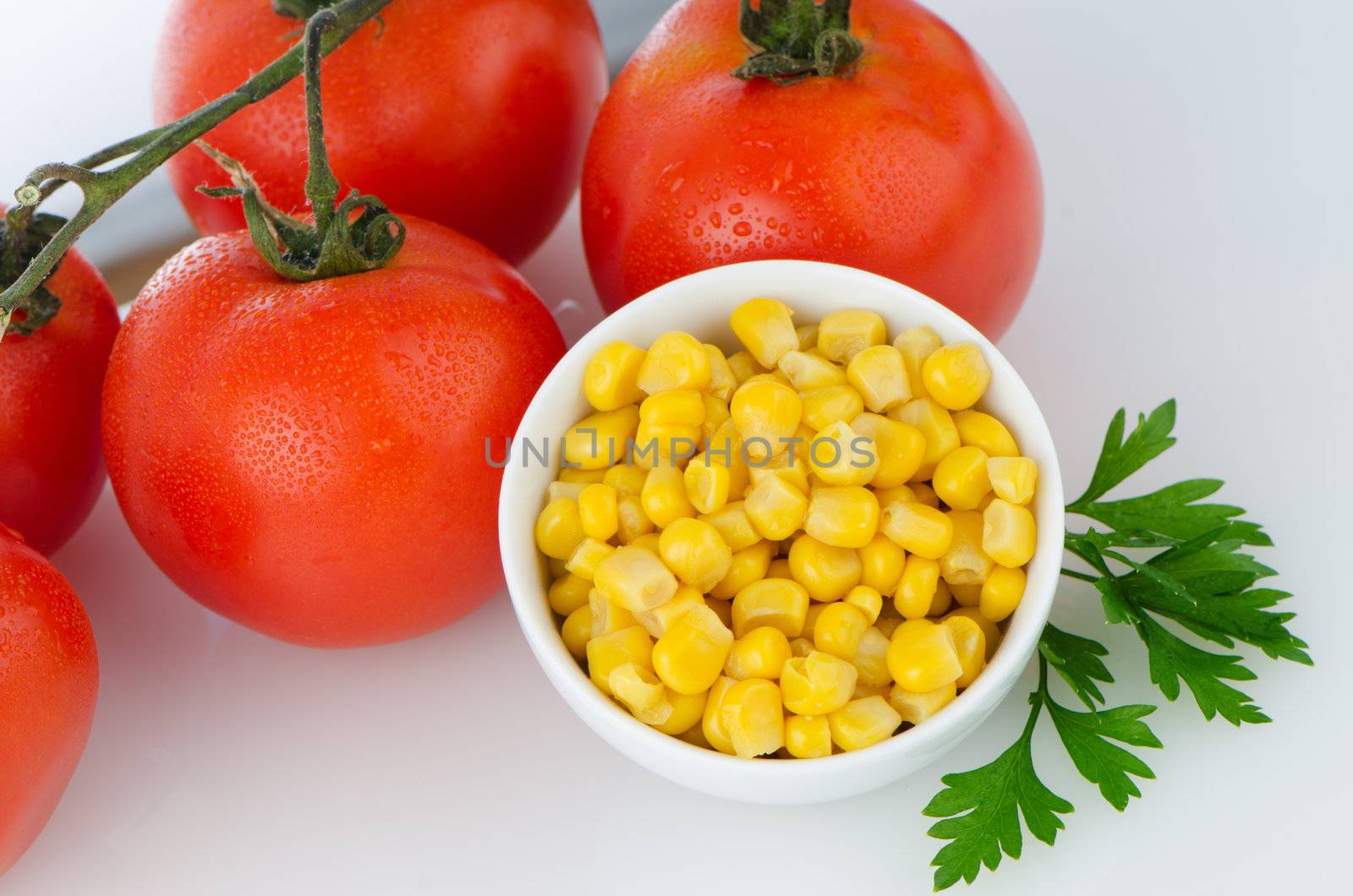 Corn grains on bowl and cherry tomatoes vine on white background.