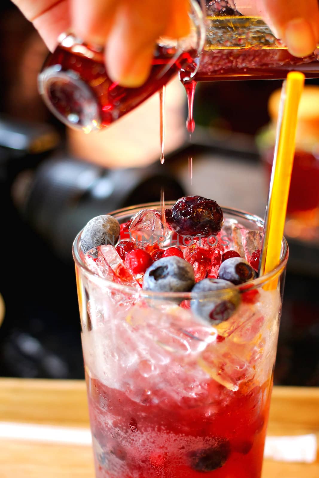 Woman hands pouring syrup over a glass of fresh fruit drink.