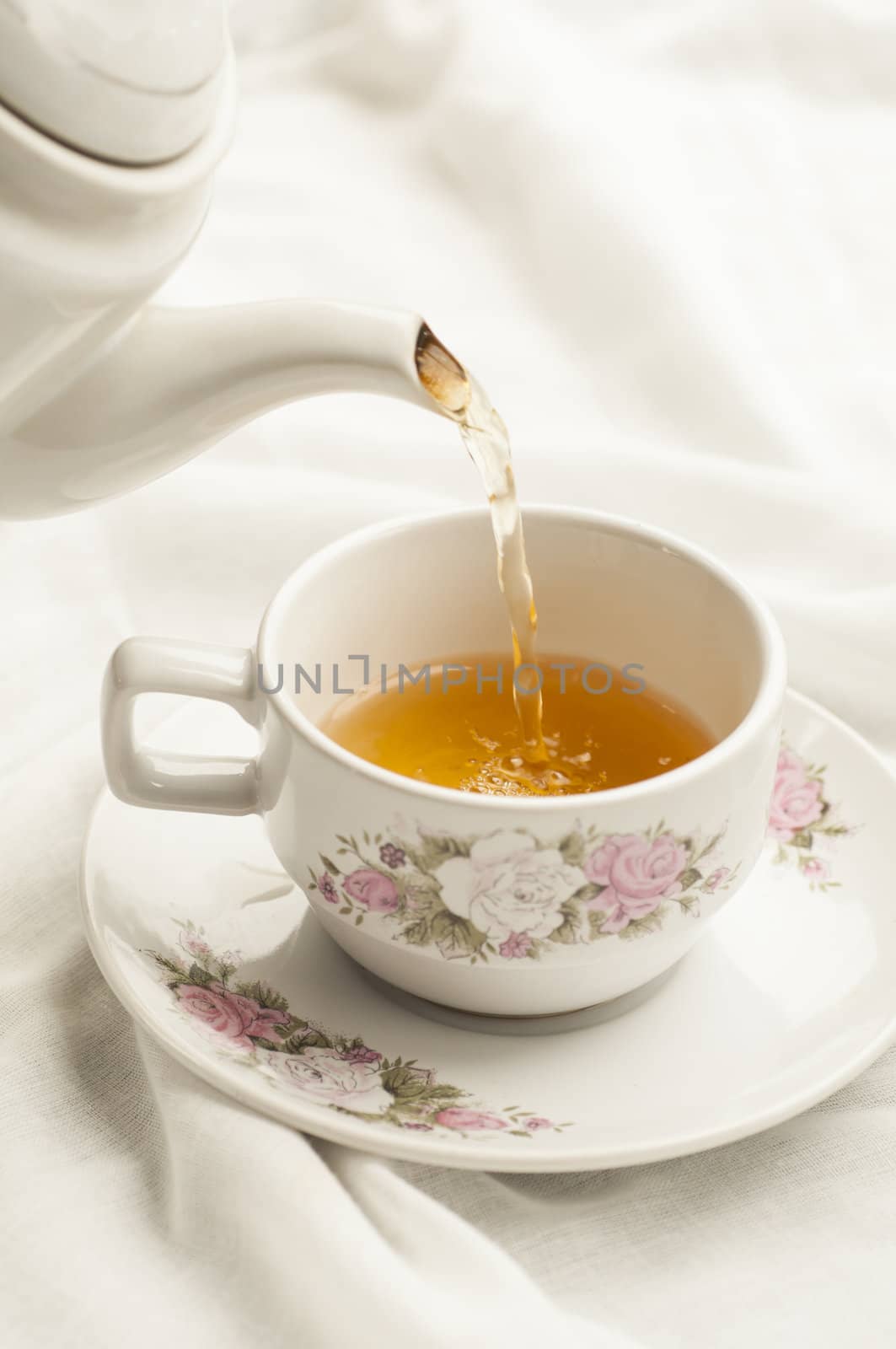Tea being poured into tea cup  on white cloth background