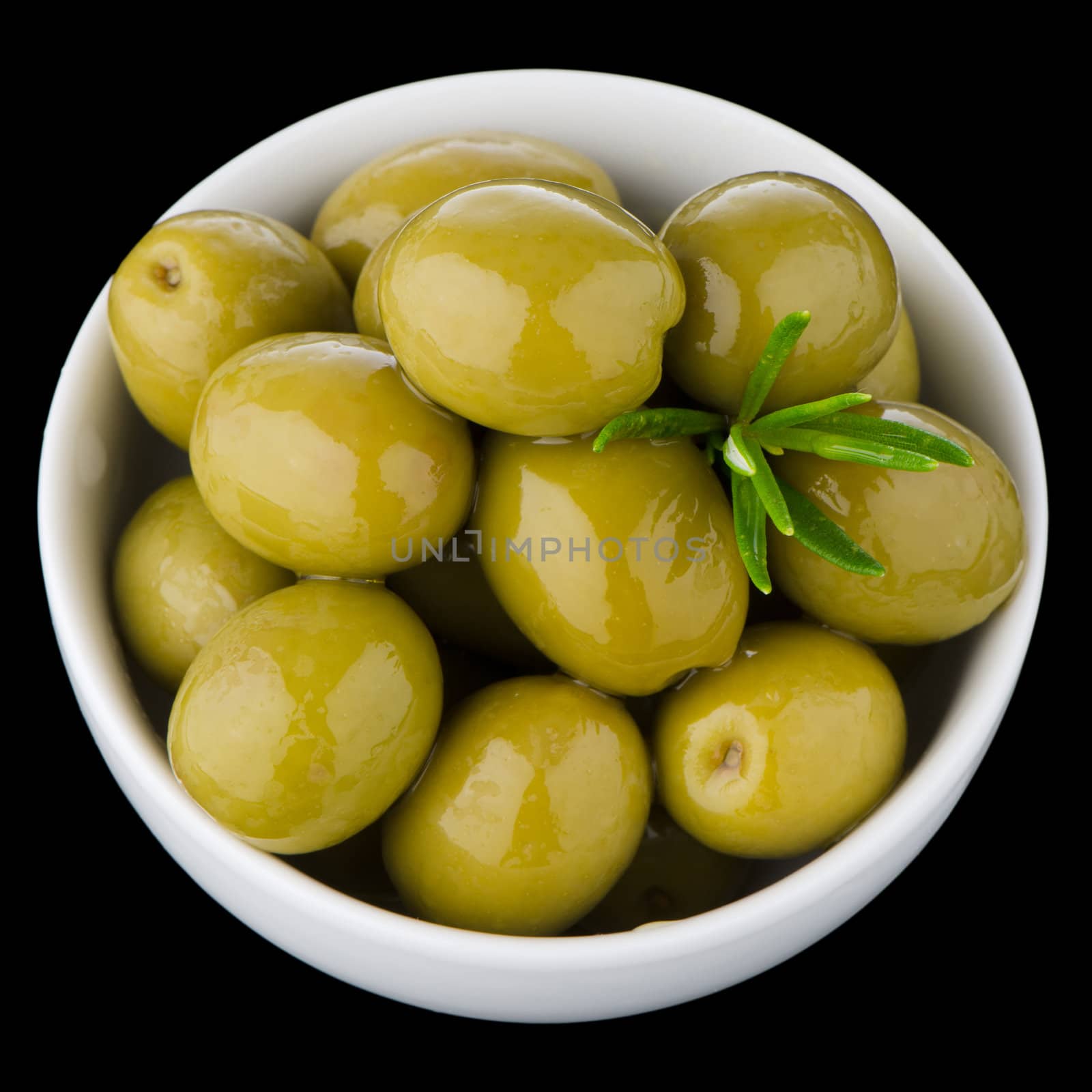 Green olives in a white ceramic bowl on black background.