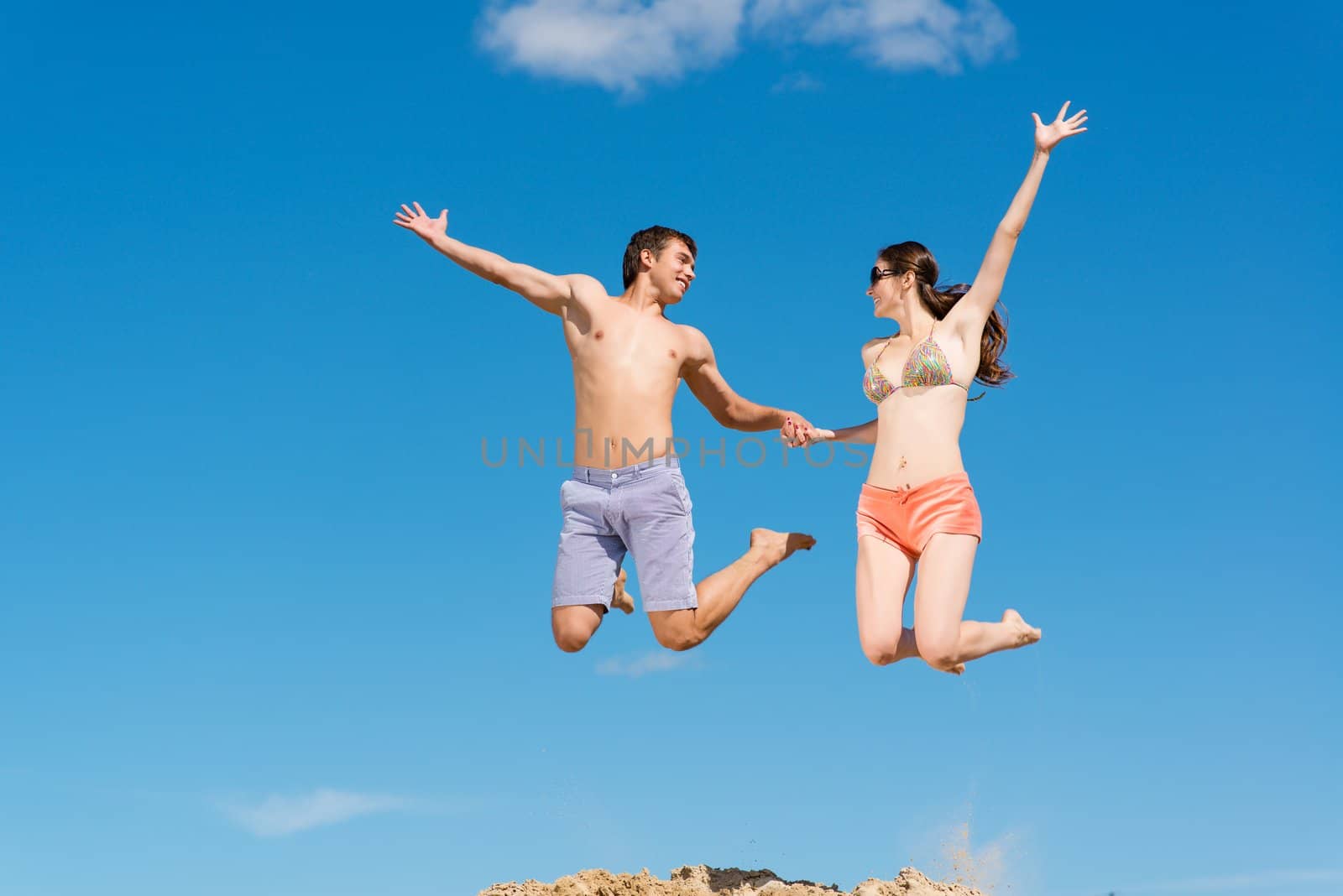 couple jumping together holding hands on a background of blue sky